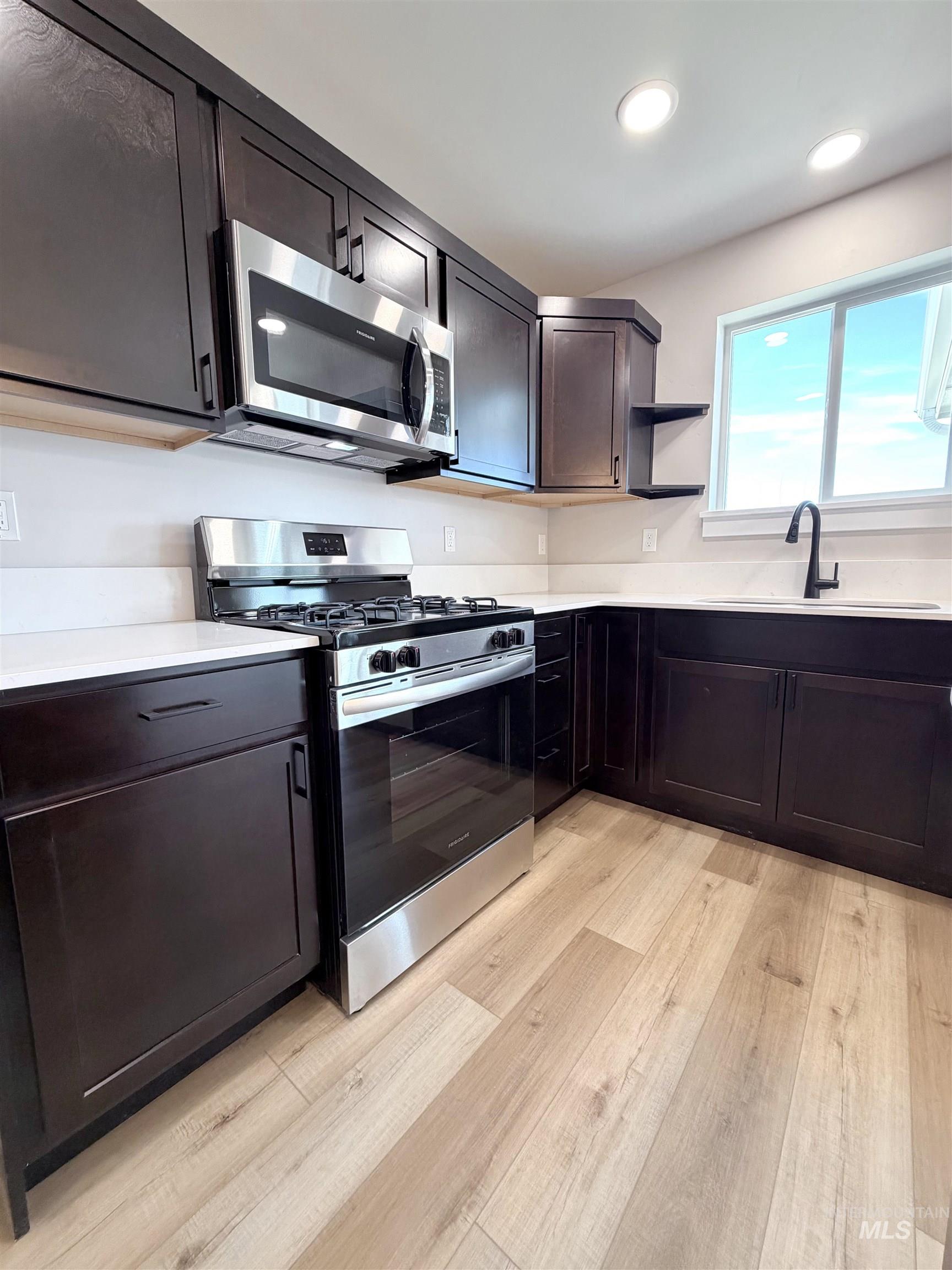 Kitchen featuring appliances with stainless steel finishes, open shelves, dark brown cabinets, light wood-type flooring, and recessed lighting