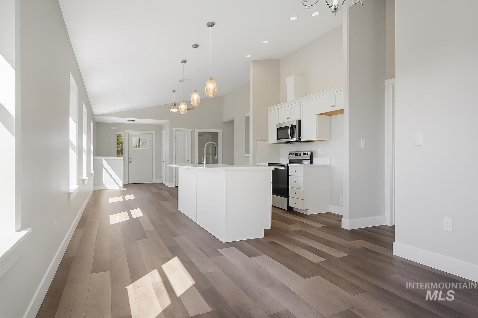 Kitchen with white cabinets, stainless steel appliances, light countertops, hanging light fixtures, and high vaulted ceiling