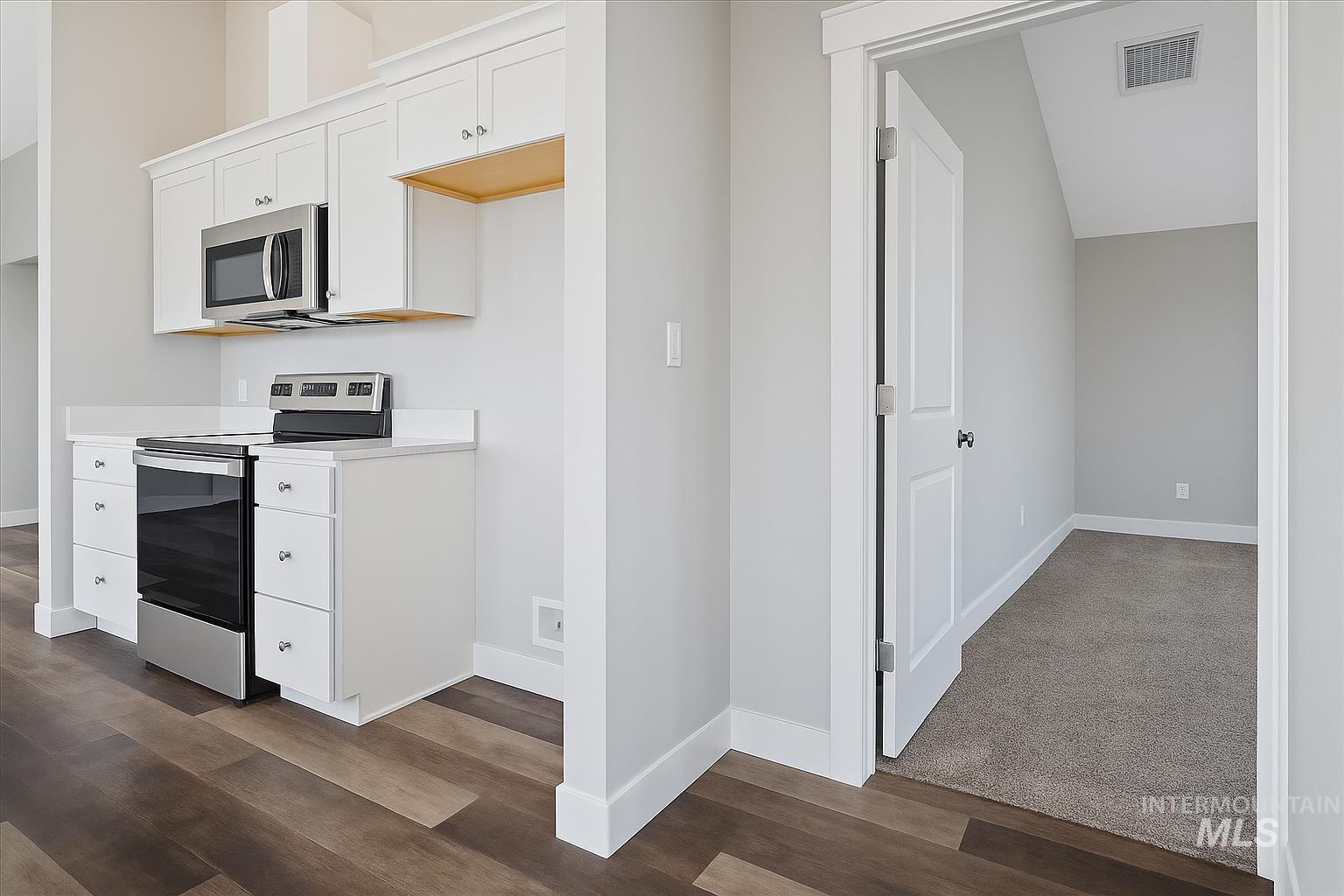 Kitchen with appliances with stainless steel finishes, white cabinetry, light countertops, and dark wood-style flooring