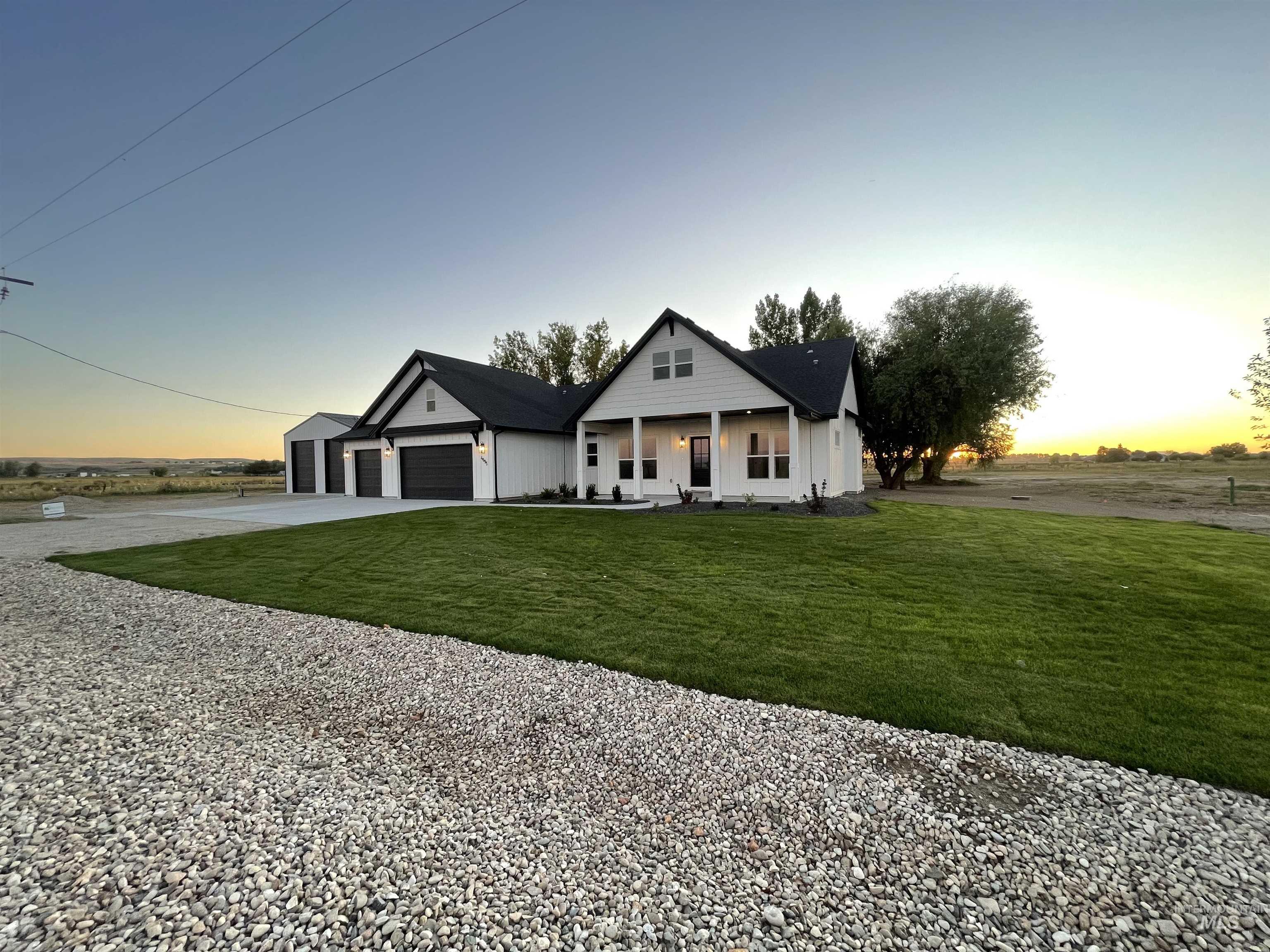 Modern farmhouse style home with a front yard, covered porch, gravel driveway, and an attached garage