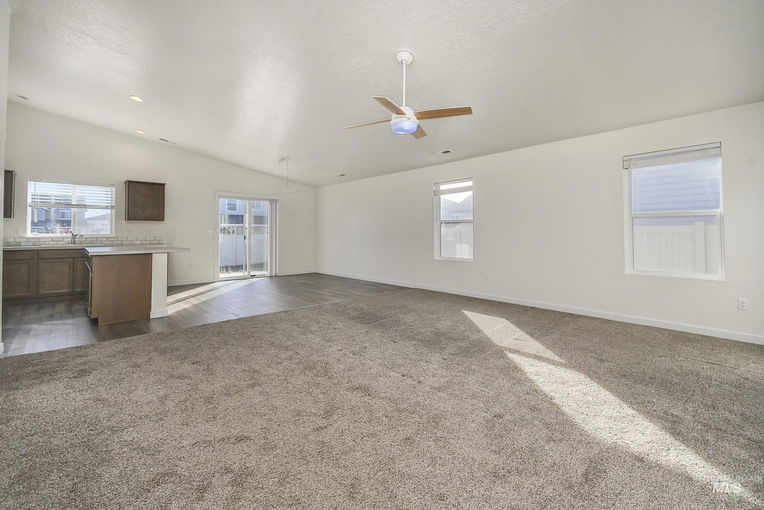 Unfurnished living room with vaulted ceiling, dark colored carpet, and a ceiling fan