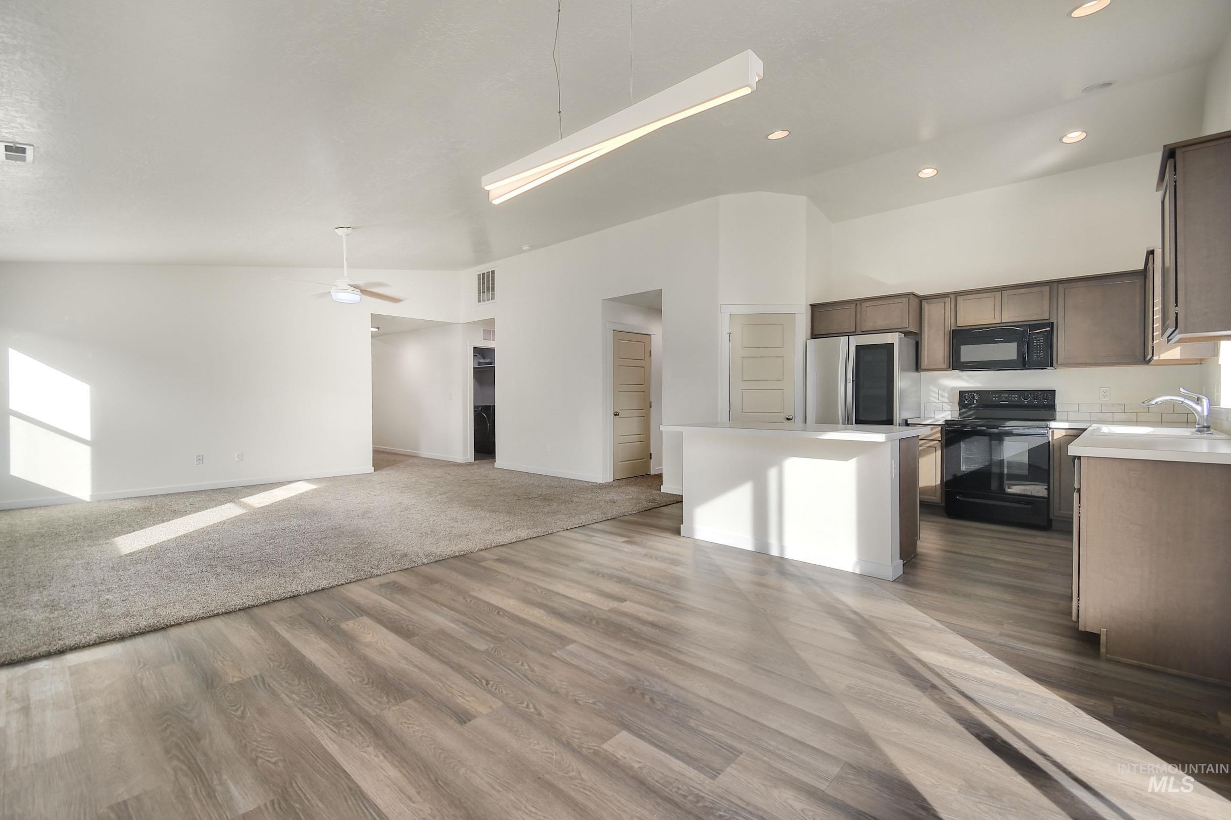 Kitchen featuring open floor plan, black appliances, light countertops, a center island, and ceiling fan