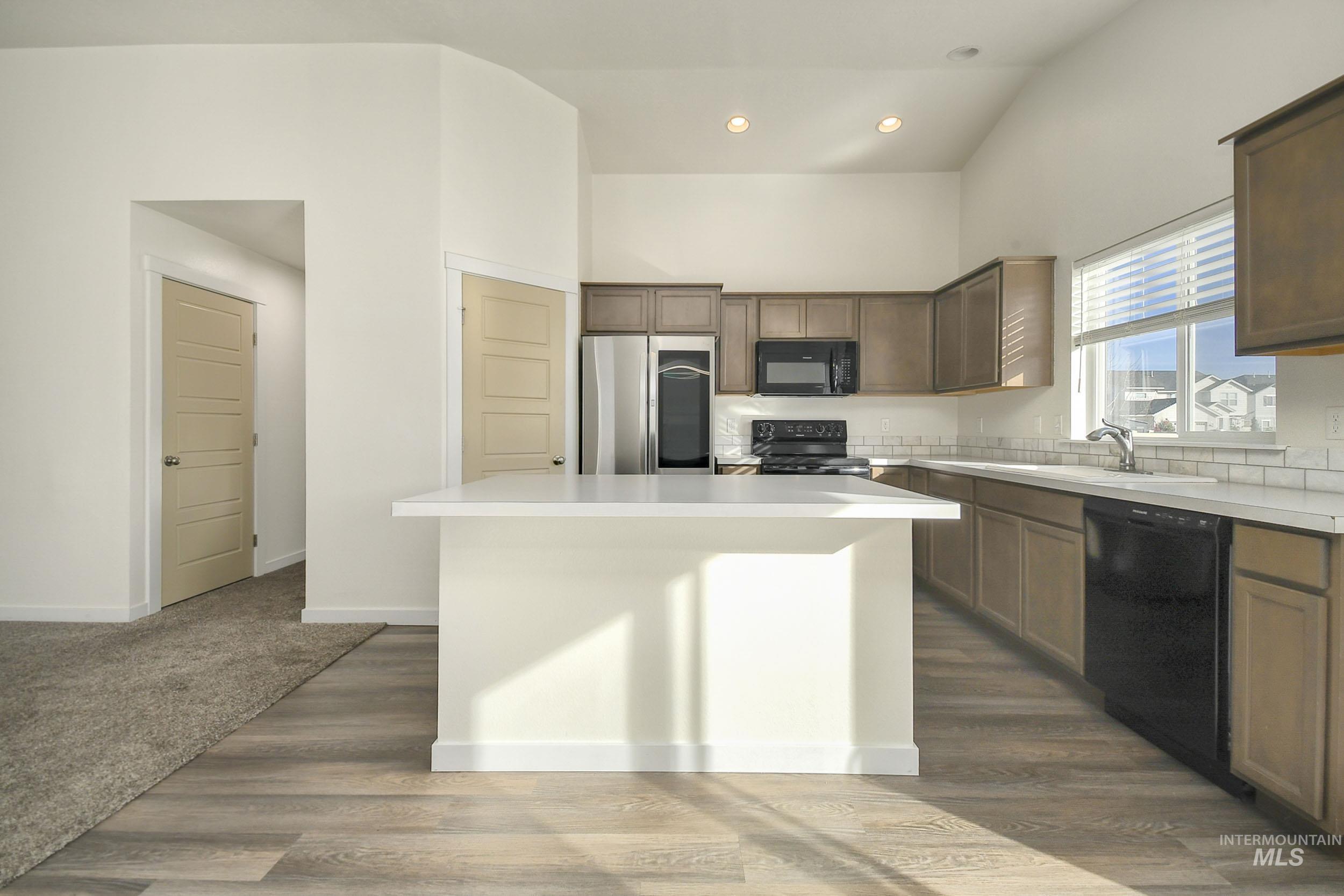 Kitchen with light countertops, black appliances, a kitchen island, dark wood finished floors, and recessed lighting