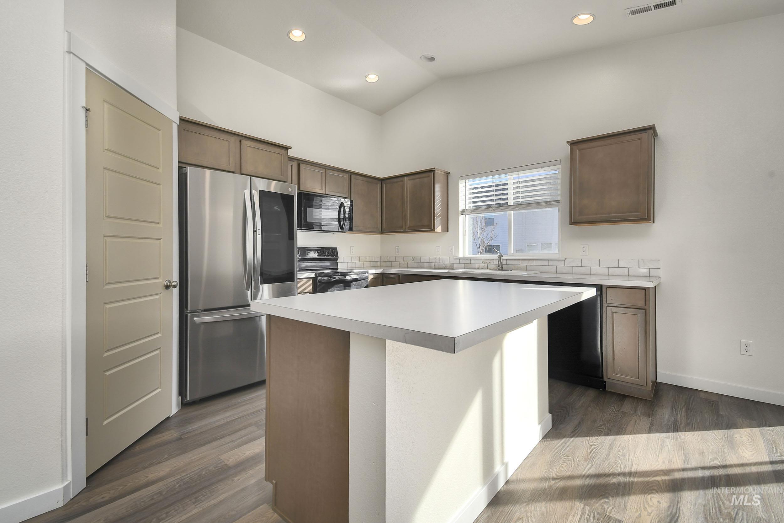 Kitchen featuring black appliances, light countertops, a kitchen island, dark wood finished floors, and dark brown cabinets