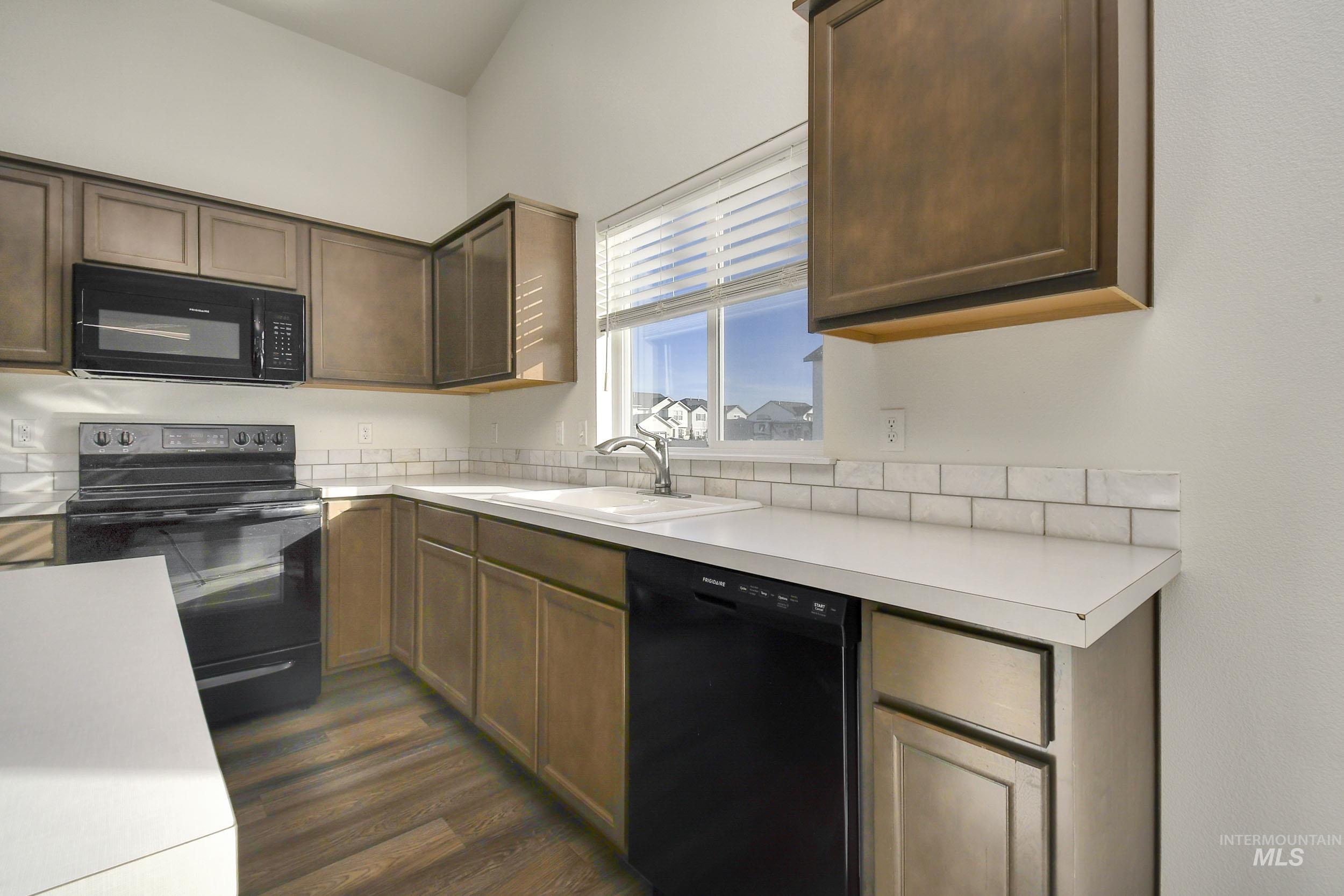 Kitchen featuring black appliances, light countertops, dark wood-style floors, and dark brown cabinetry