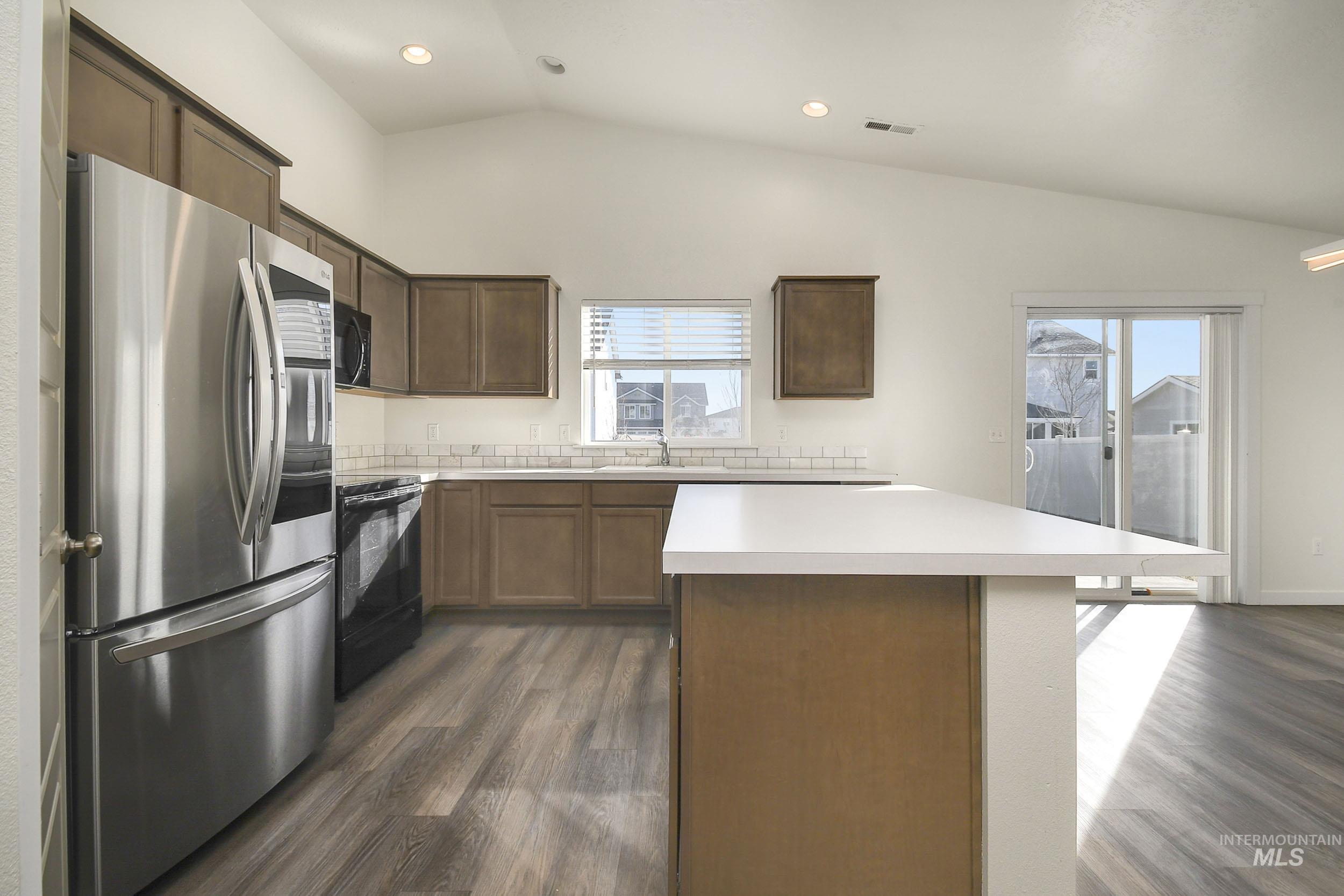 Kitchen with black appliances, lofted ceiling, light countertops, a kitchen island, and dark wood-style floors