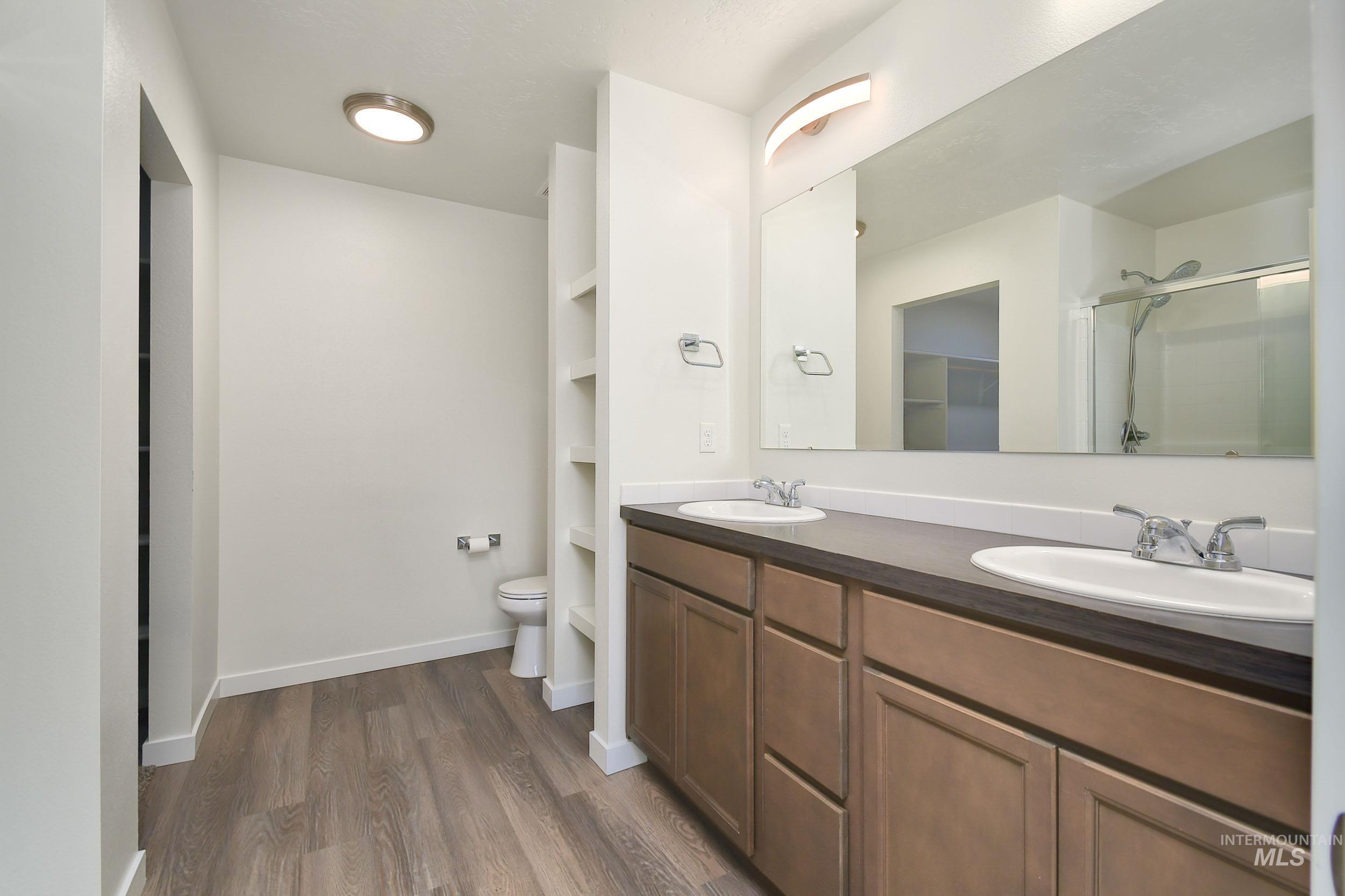 Bathroom featuring double vanity, dark wood-type flooring, a shower stall, and a walk in closet