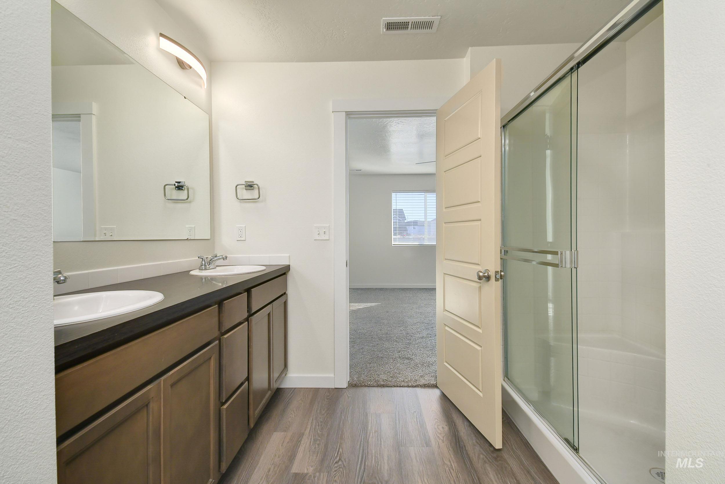 Full bathroom featuring double vanity, a stall shower, and dark wood-style floors