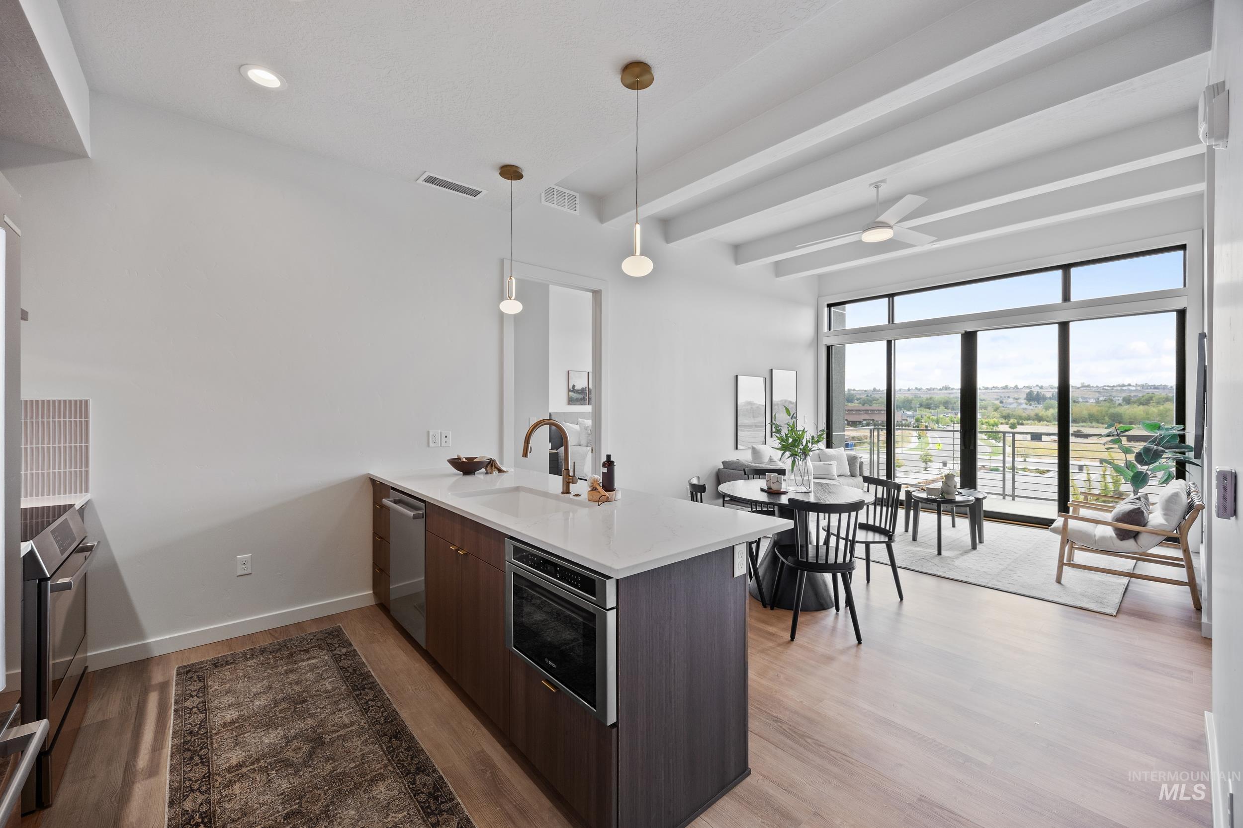 Kitchen featuring modern cabinets, a peninsula, light wood finished floors, hanging light fixtures, and beamed ceiling