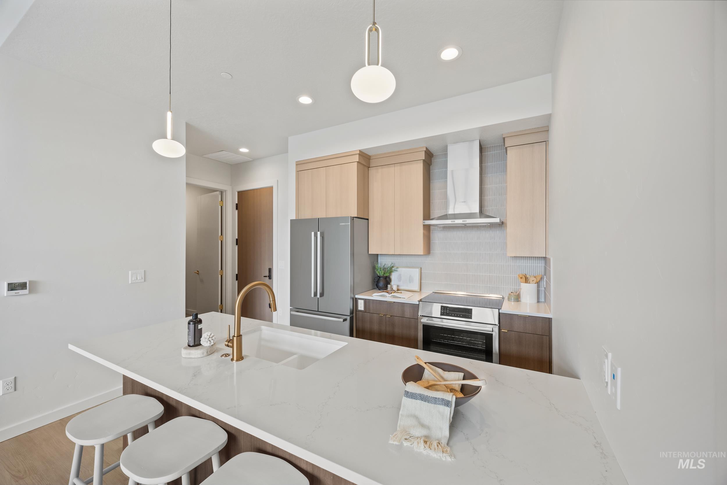 Kitchen with backsplash, pendant lighting, light stone counters, modern cabinets, and wall chimney exhaust hood
