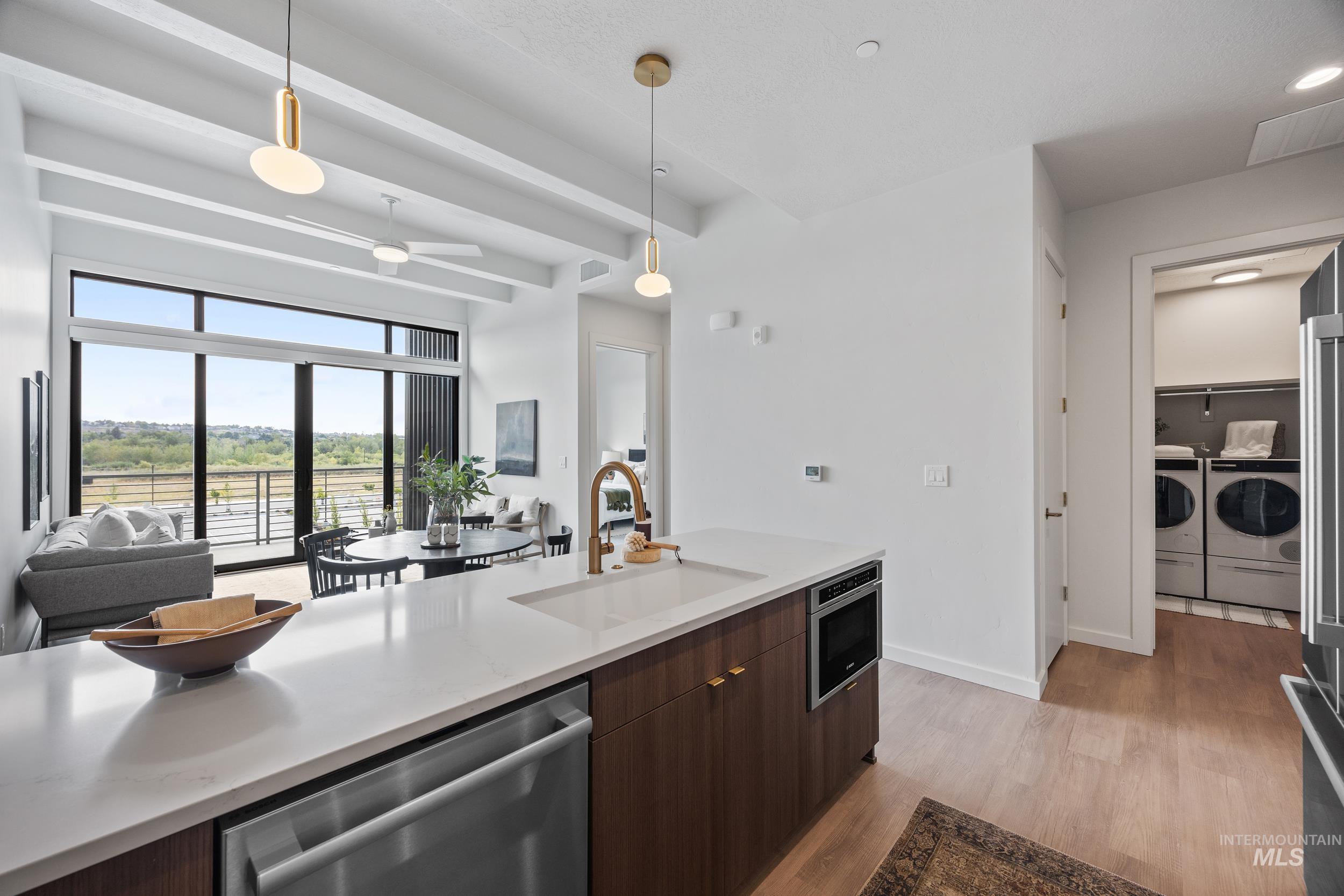 Kitchen with stainless steel appliances, open floor plan, dark brown cabinets, pendant lighting, and light wood finished floors