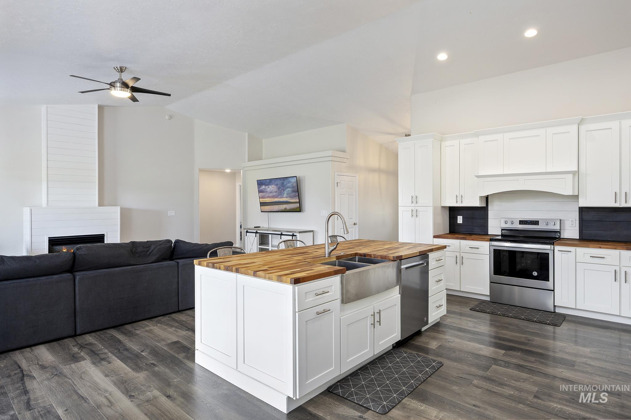 Kitchen with open floor plan, white cabinetry, appliances with stainless steel finishes, a kitchen island with sink, and high vaulted ceiling
