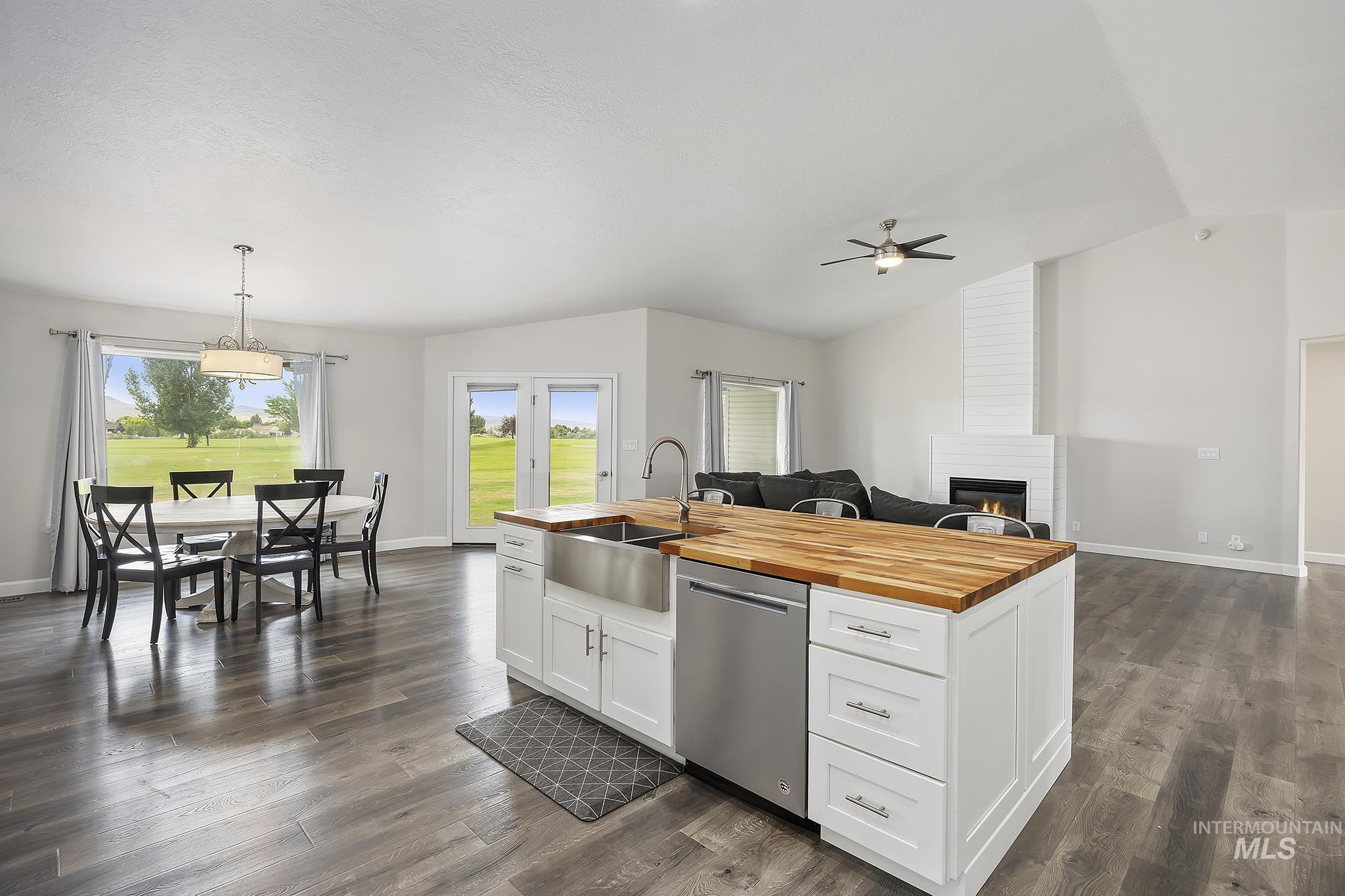 Kitchen with butcher block counters, white cabinets, open floor plan, stainless steel dishwasher, and lofted ceiling