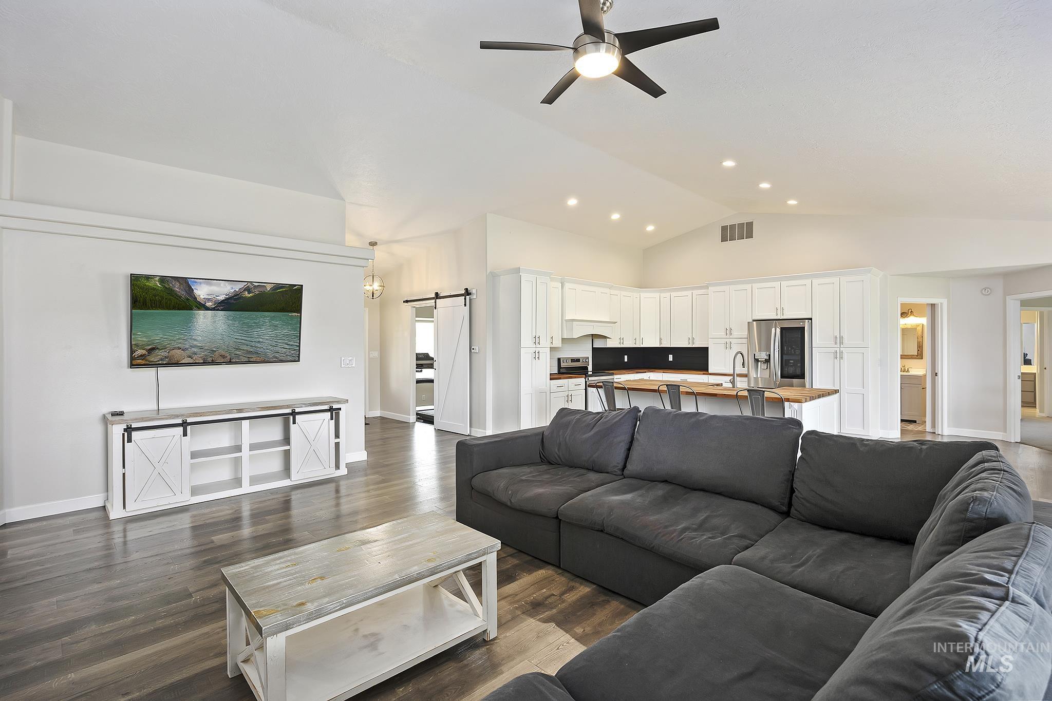 Living area with a barn door, vaulted ceiling, dark wood-style flooring, and ceiling fan