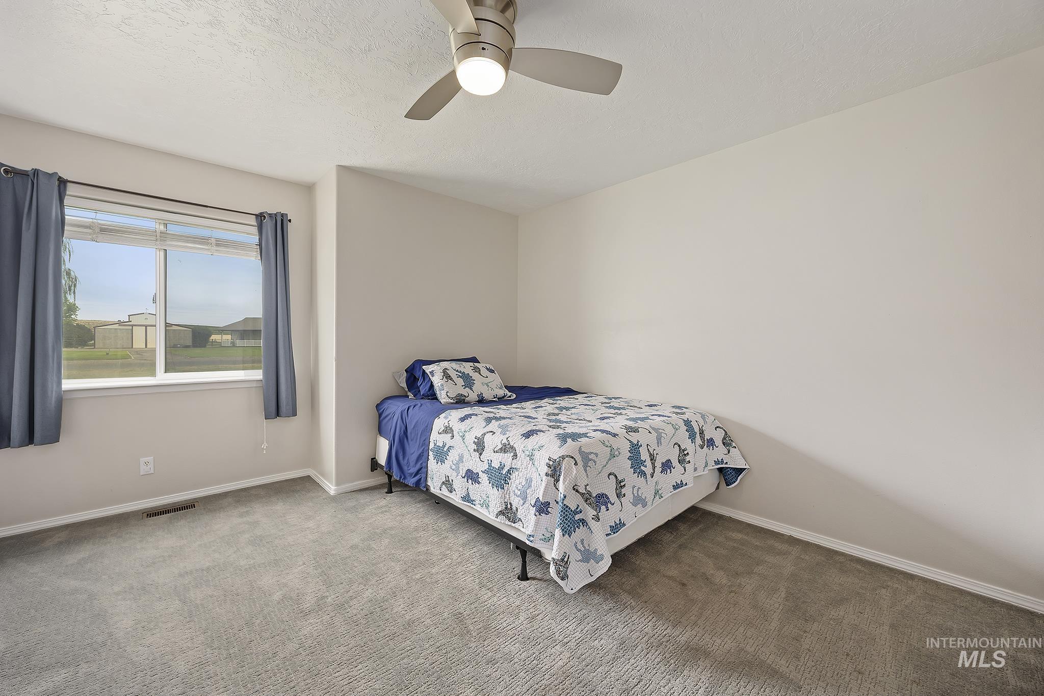 Bedroom with ceiling fan, carpet floors, and a textured ceiling
