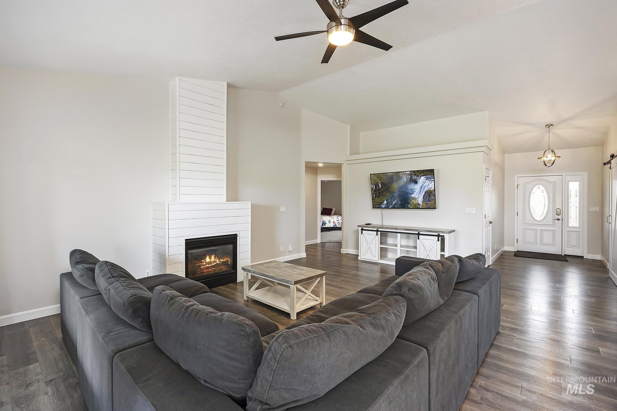Living area featuring lofted ceiling, dark wood-style flooring, a large fireplace, and a ceiling fan
