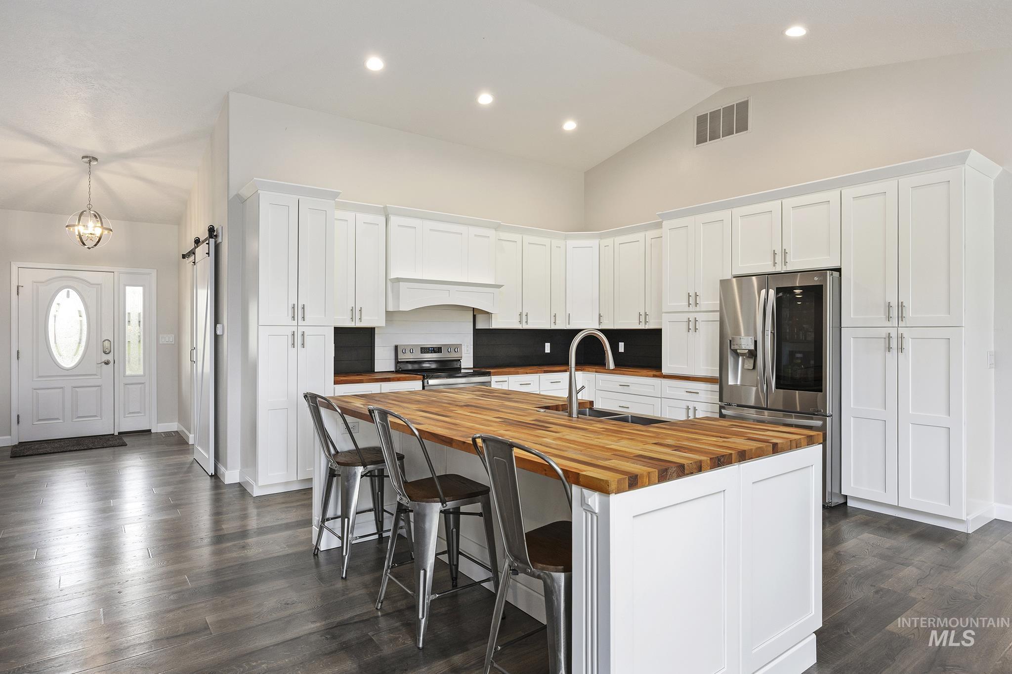 Kitchen featuring a barn door, white cabinetry, appliances with stainless steel finishes, a kitchen island with sink, and a breakfast bar area