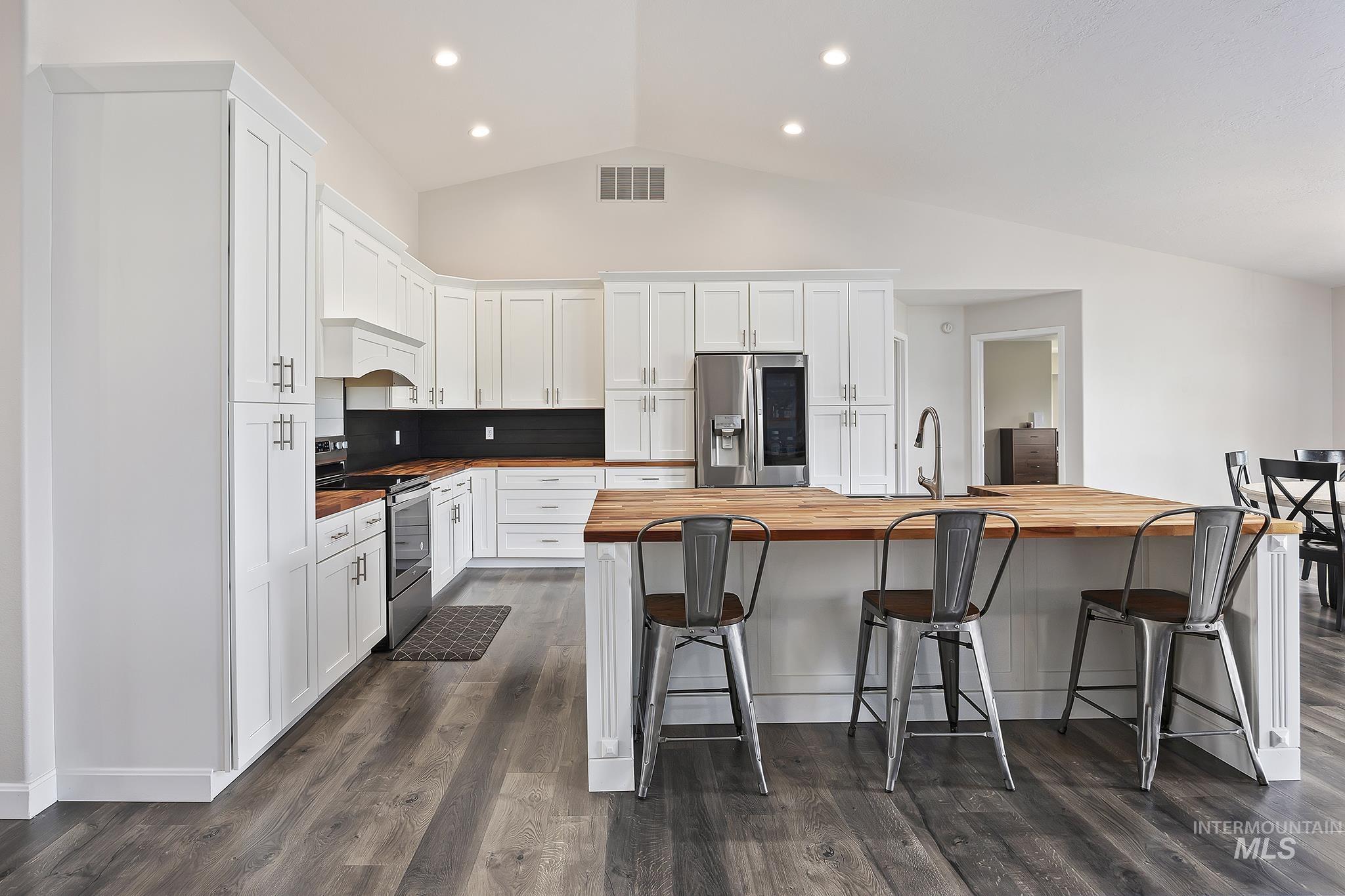 Kitchen featuring butcher block countertops, white cabinets, stainless steel appliances, vaulted ceiling, and dark wood-style flooring