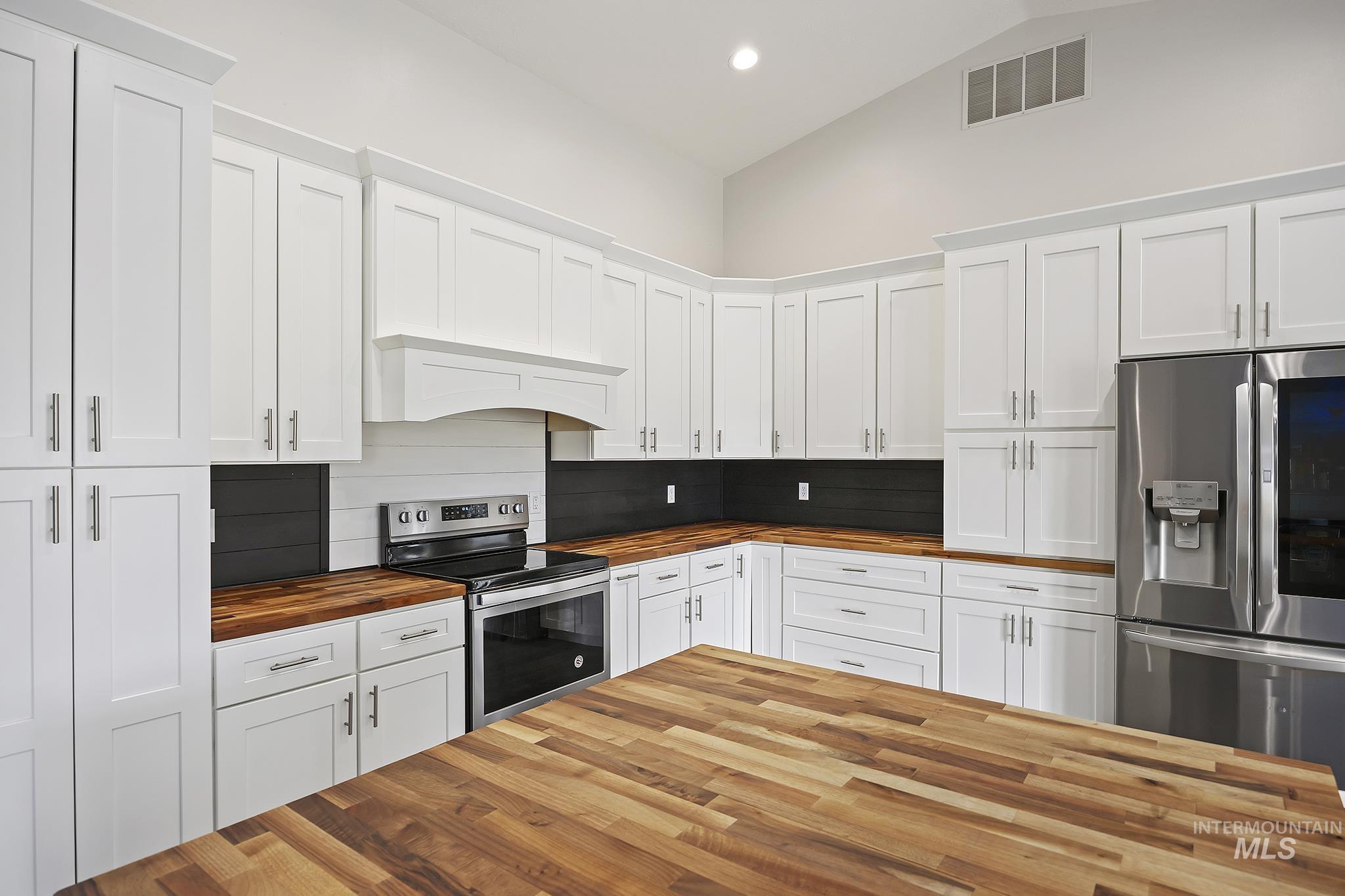 Kitchen with butcher block countertops, white cabinets, stainless steel appliances, recessed lighting, and high vaulted ceiling