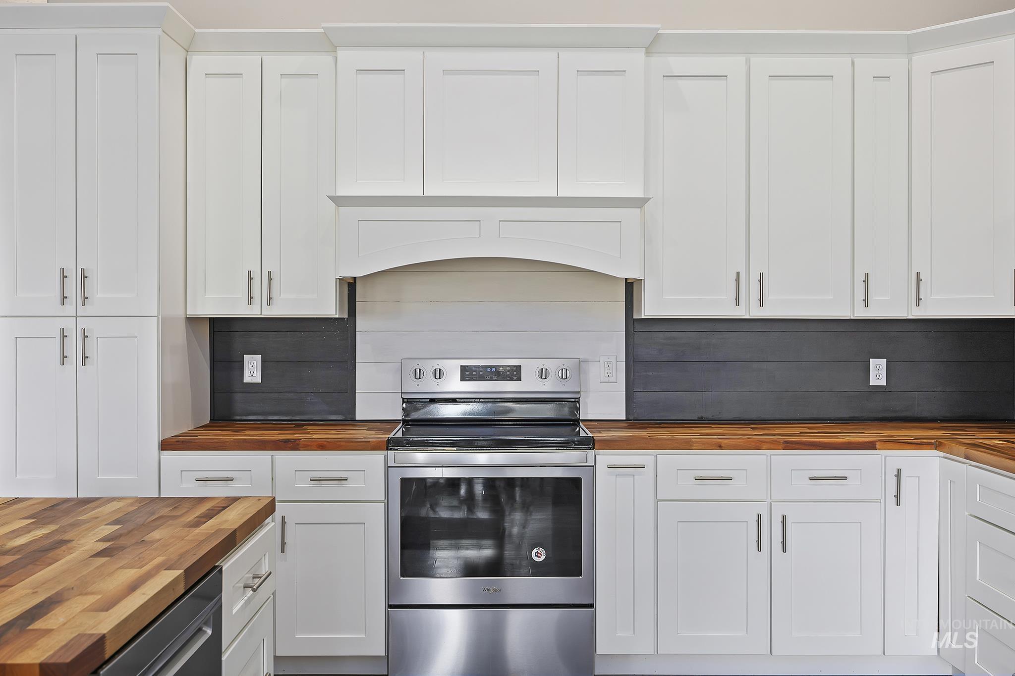 Kitchen with wooden counters, appliances with stainless steel finishes, and white cabinets