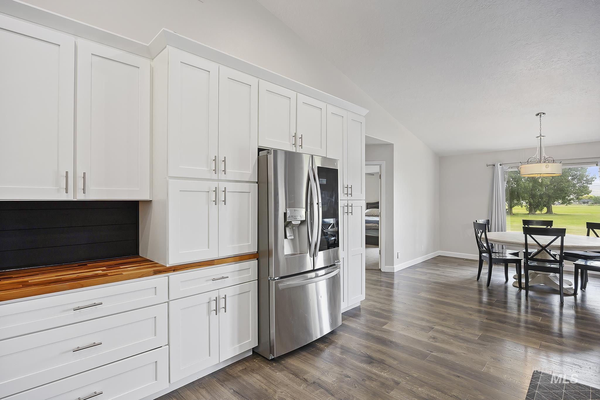 Kitchen with white cabinetry, stainless steel refrigerator with ice dispenser, vaulted ceiling, butcher block countertops, and decorative light fixtures