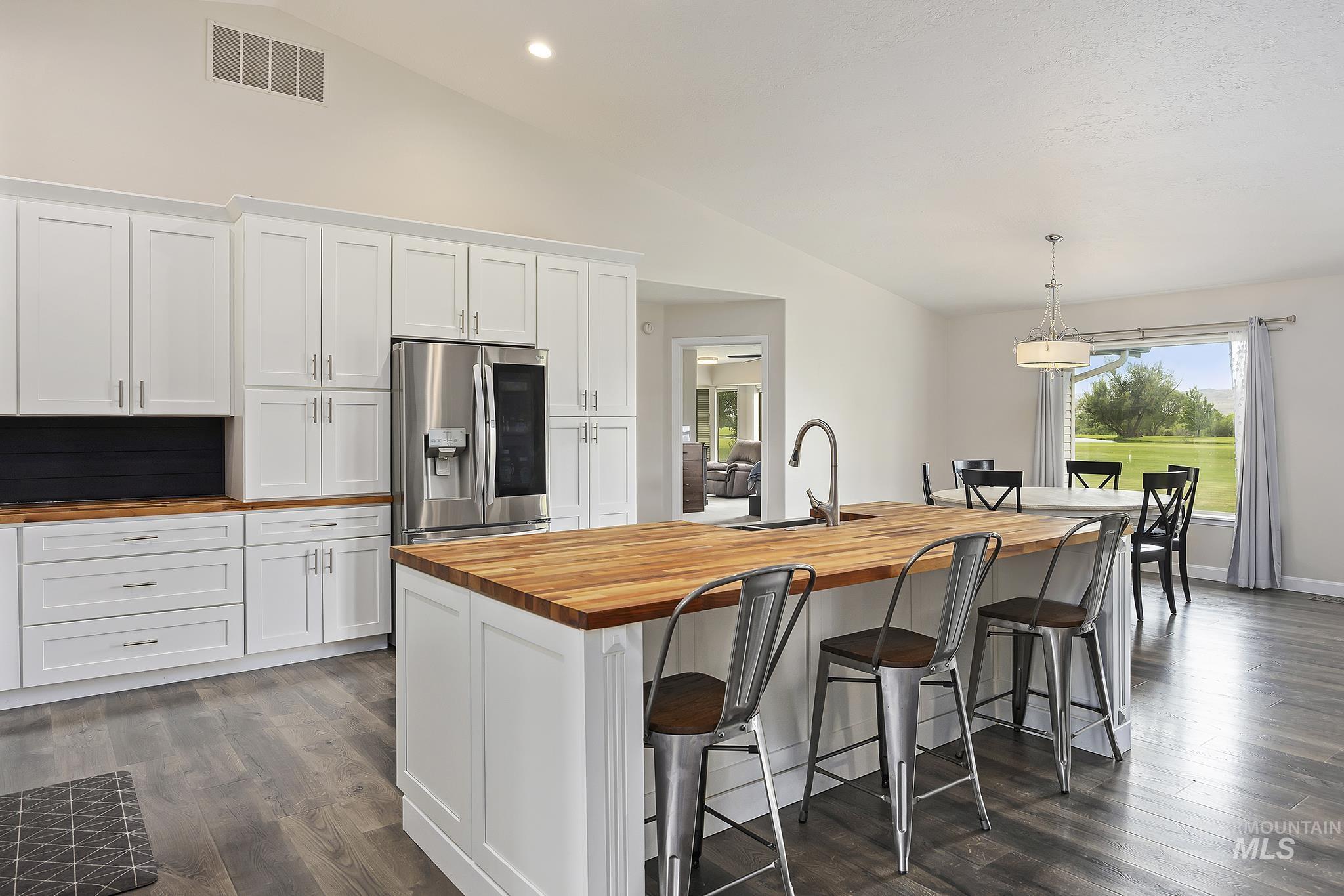Kitchen featuring white cabinets, wood counters, stainless steel fridge, recessed lighting, and high vaulted ceiling