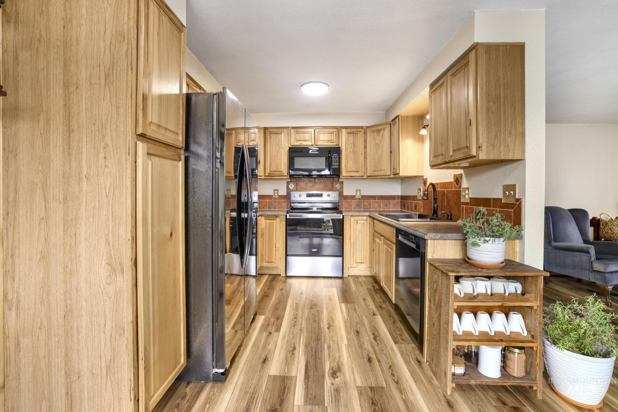 Kitchen with black appliances, light wood-type flooring, light brown cabinetry, and dark countertops