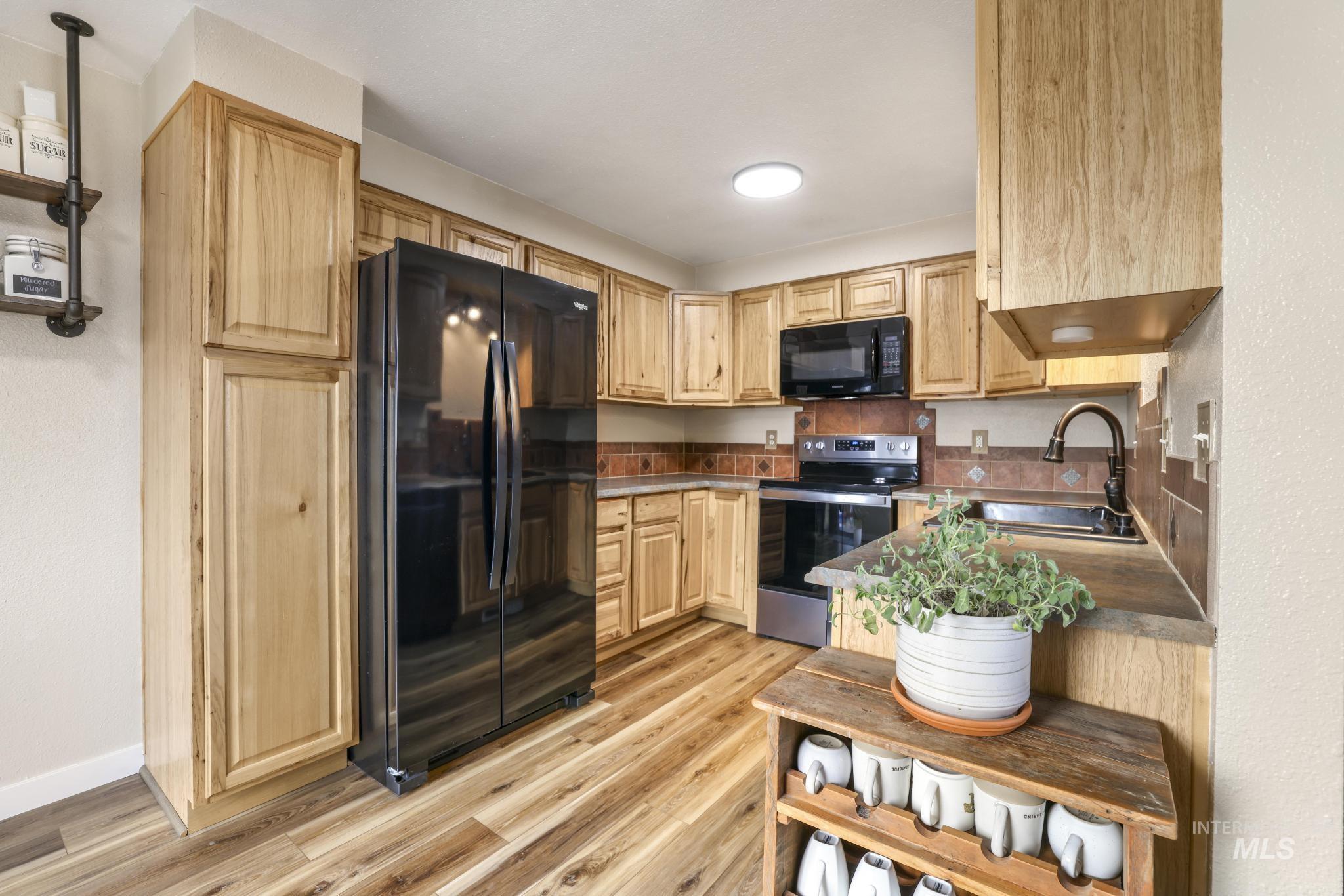 Kitchen with black appliances, light brown cabinetry, and light wood-type flooring