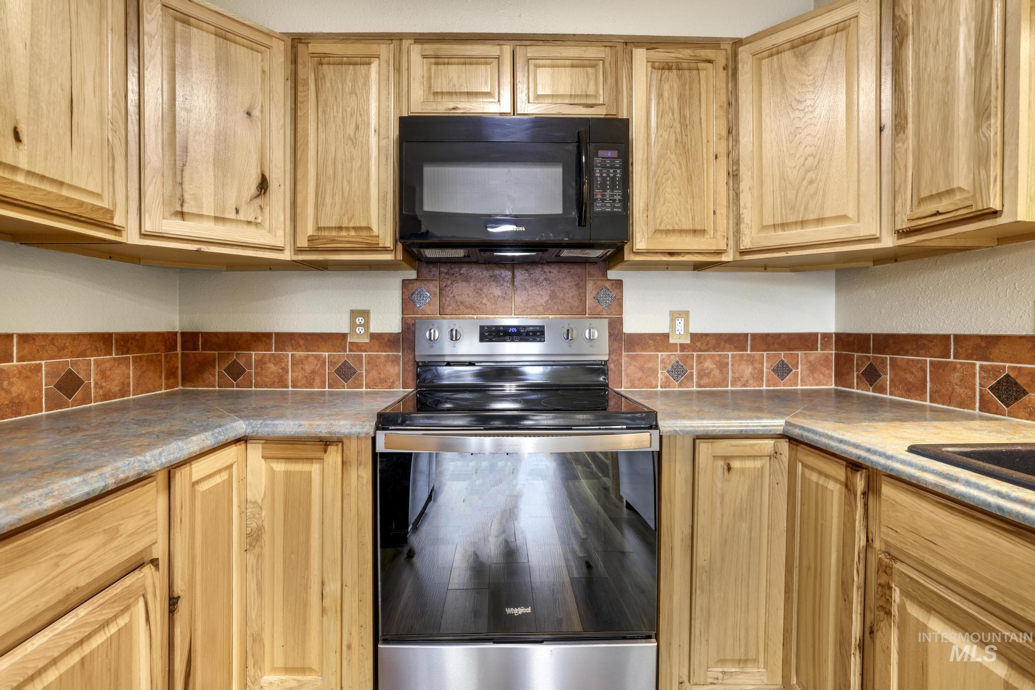 Kitchen with stainless steel range with electric stovetop, black microwave, and decorative backsplash