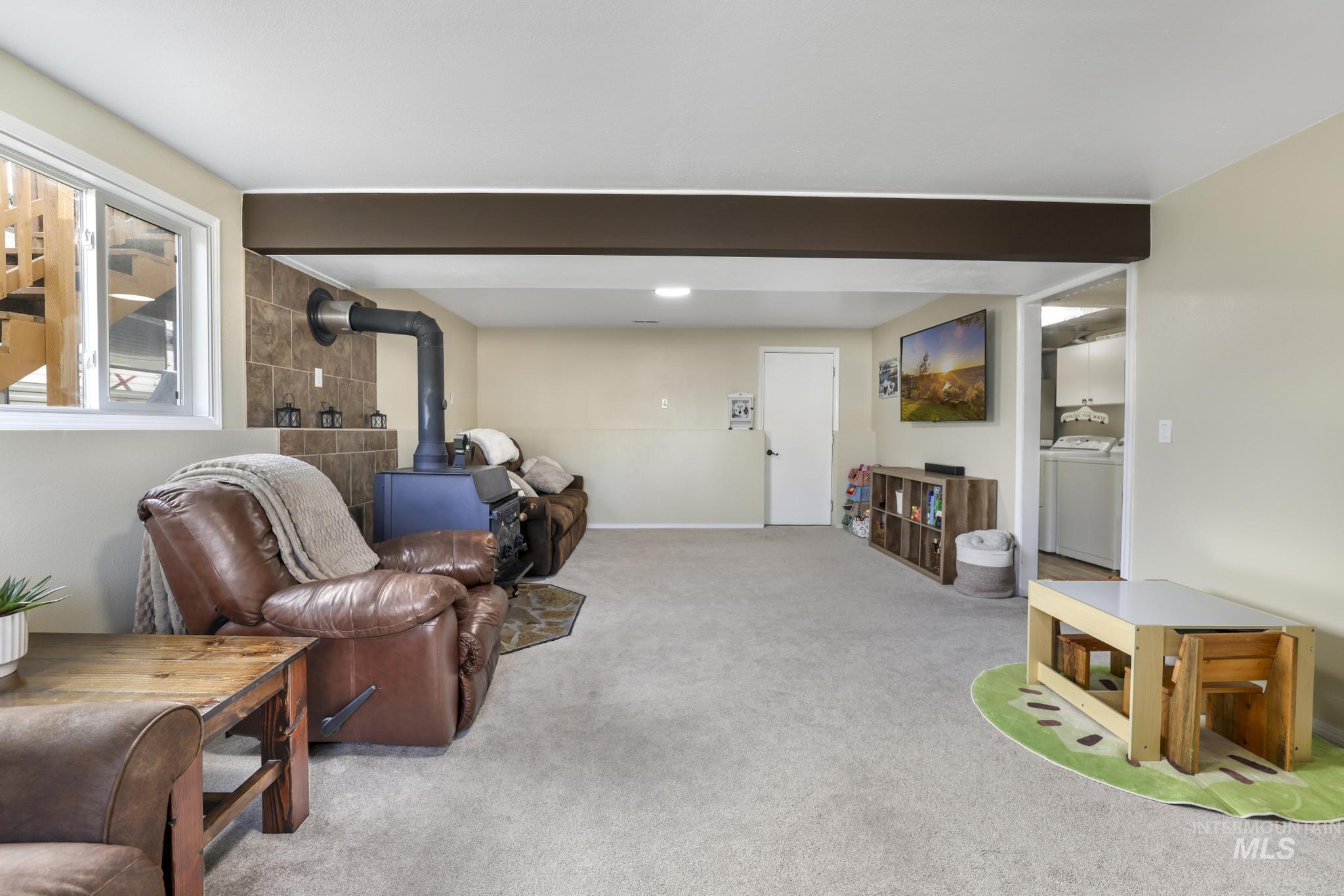 Carpeted living area featuring a wood stove, beam ceiling, and washer / clothes dryer