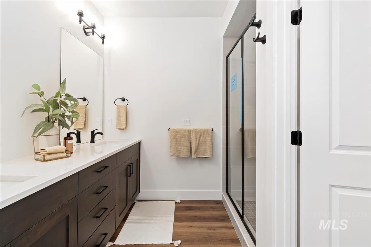 Full bathroom with double vanity, a shower stall, and dark wood finished floors