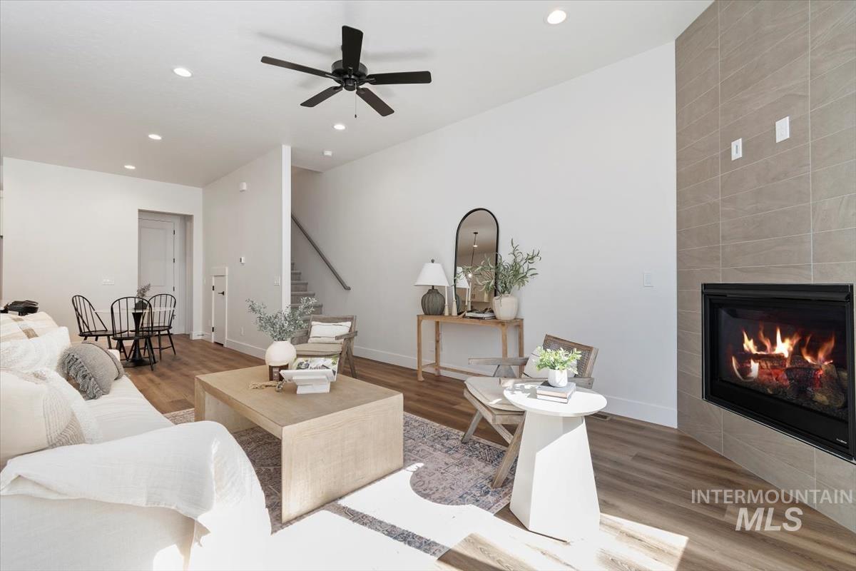 Living area with wood finished floors, a tiled fireplace, a ceiling fan, stairway, and recessed lighting