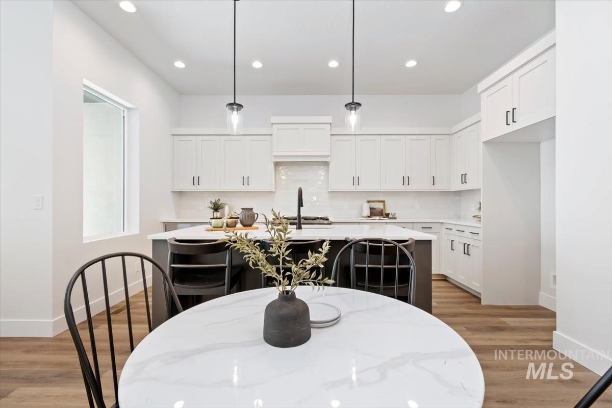 Kitchen featuring decorative light fixtures, white cabinetry, a center island with sink, recessed lighting, and light wood-style floors