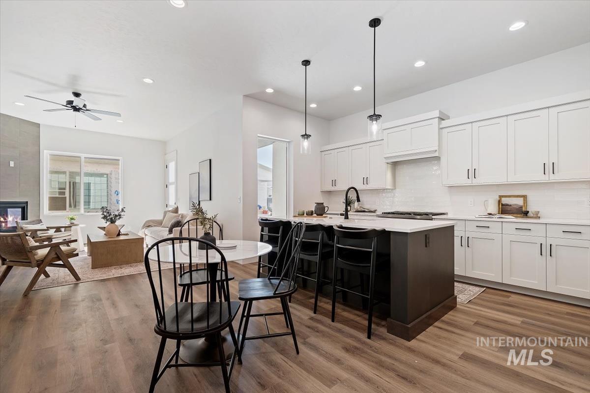 Kitchen featuring white cabinetry, a kitchen island with sink, open floor plan, a breakfast bar area, and pendant lighting