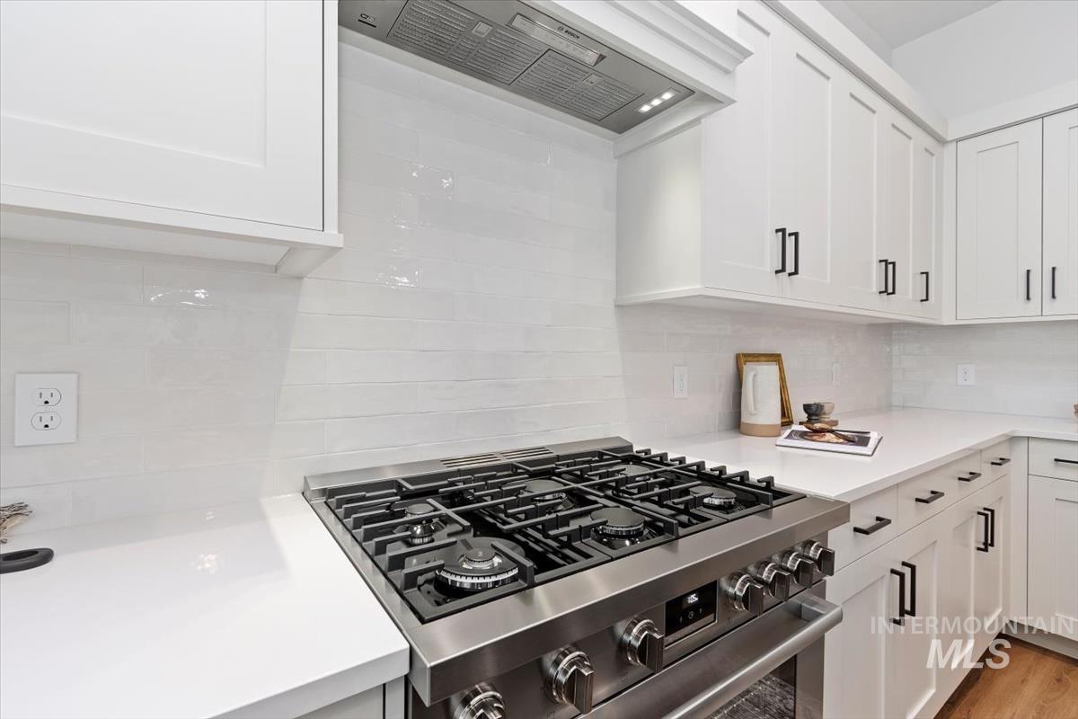 Kitchen with stainless steel gas stove, white cabinetry, custom range hood, tasteful backsplash, and light stone counters