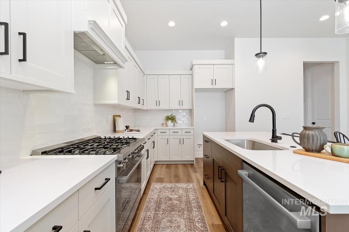 Kitchen featuring appliances with stainless steel finishes, white cabinets, recessed lighting, hanging light fixtures, and light wood-type flooring