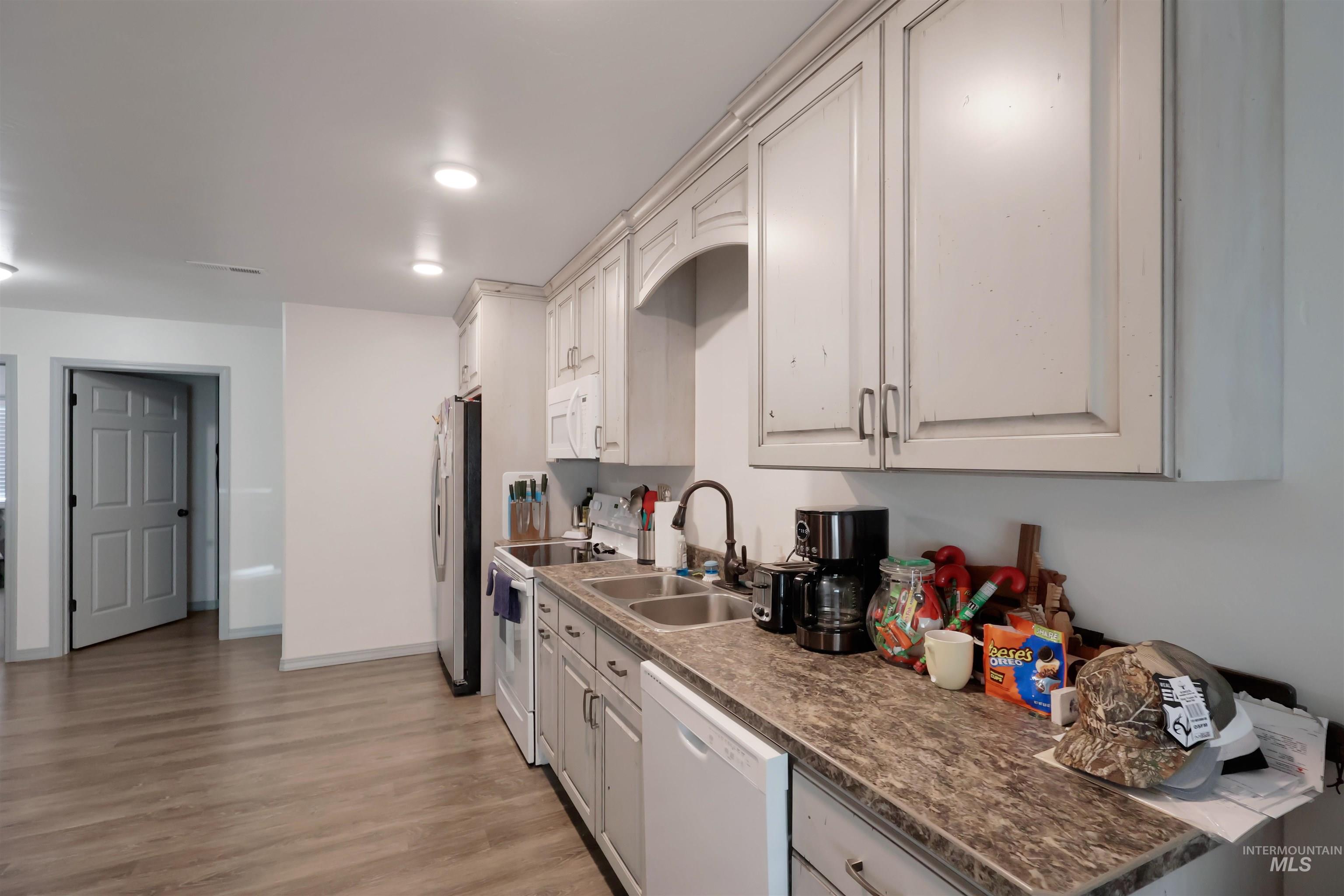 Kitchen with white appliances, light wood finished floors, dark countertops, and white cabinetry