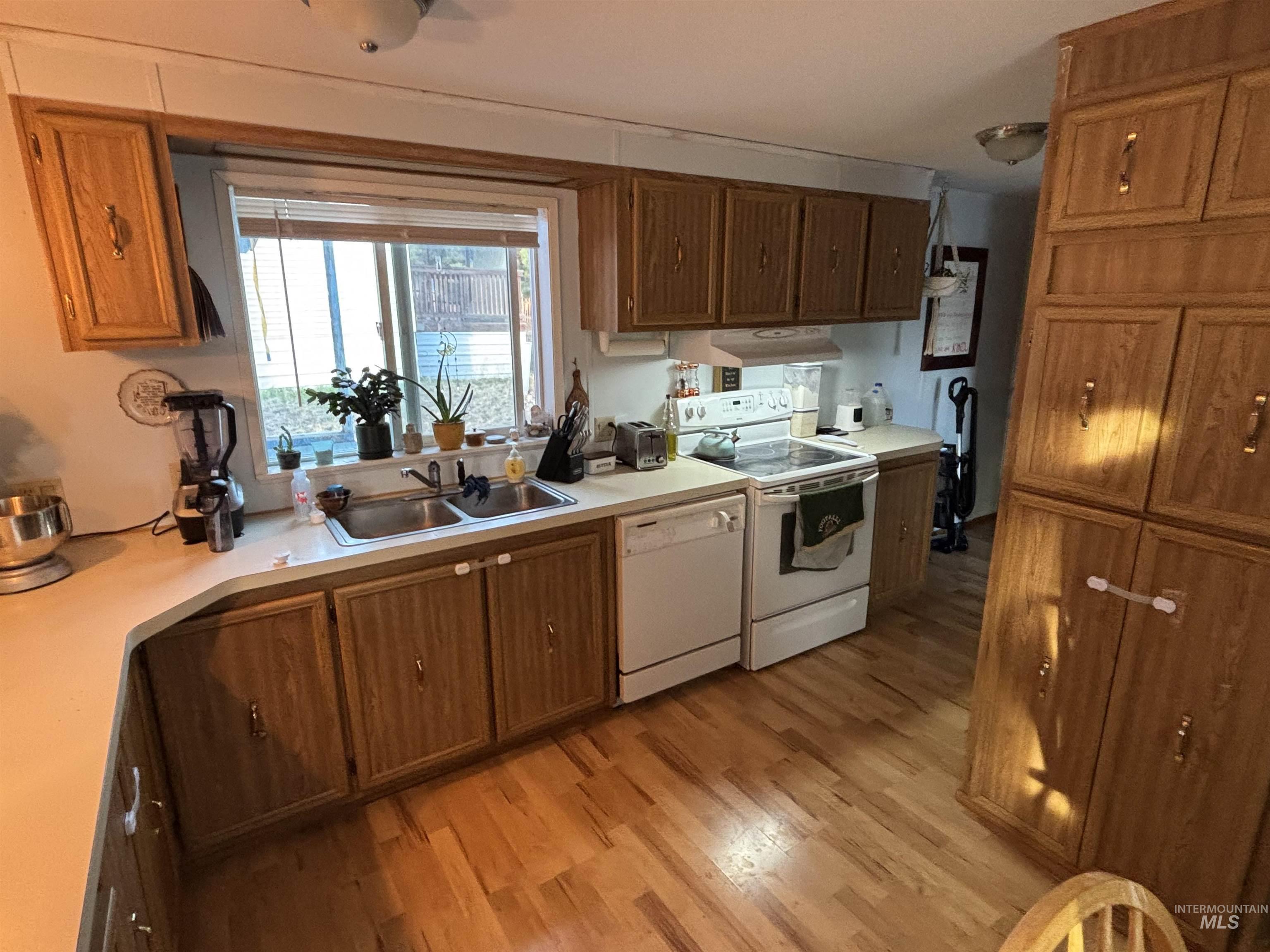 Kitchen with white appliances, light wood-style floors, brown cabinetry, light countertops, and under cabinet range hood