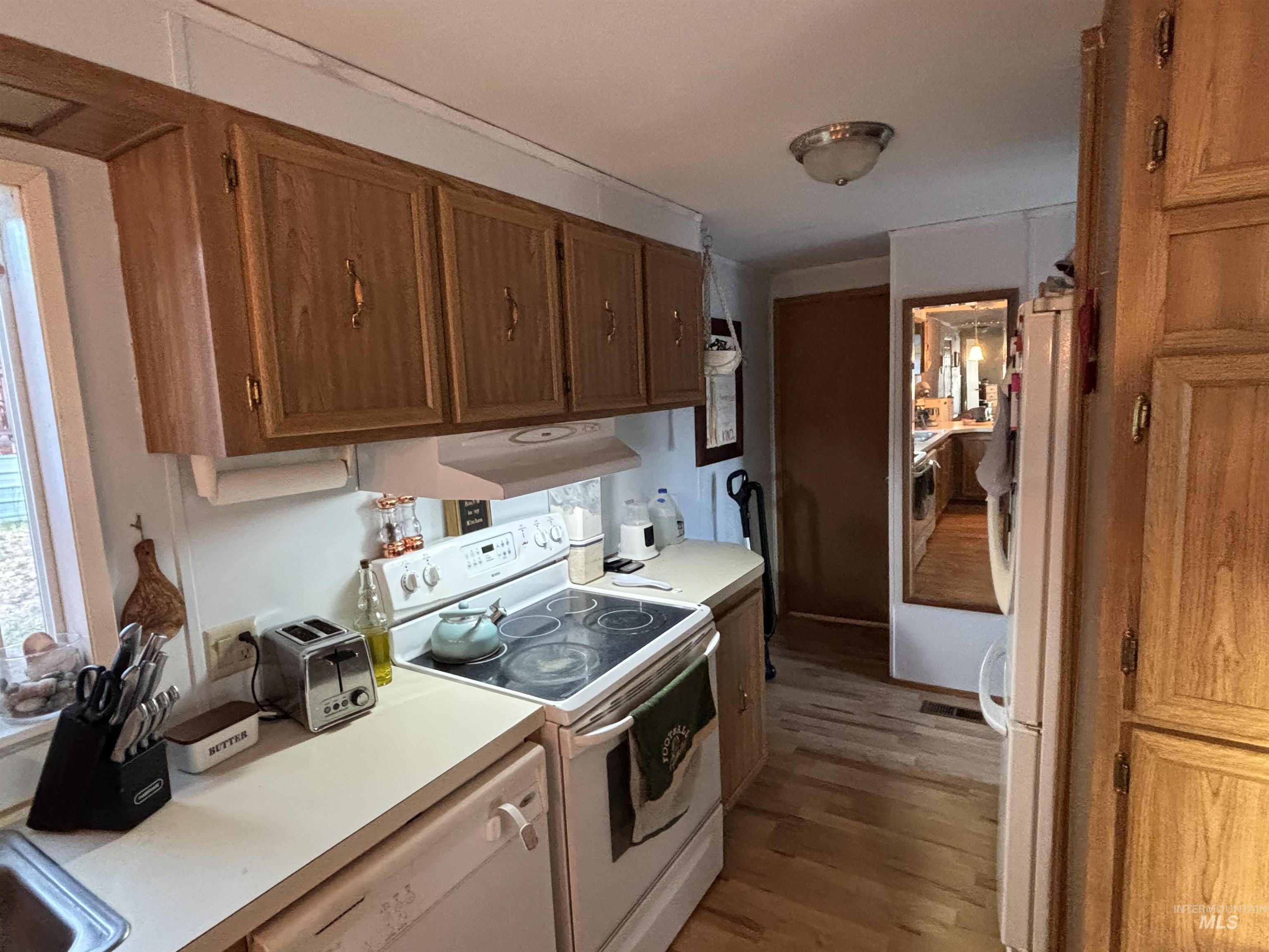 Kitchen with white appliances, wood finished floors, light countertops, and under cabinet range hood