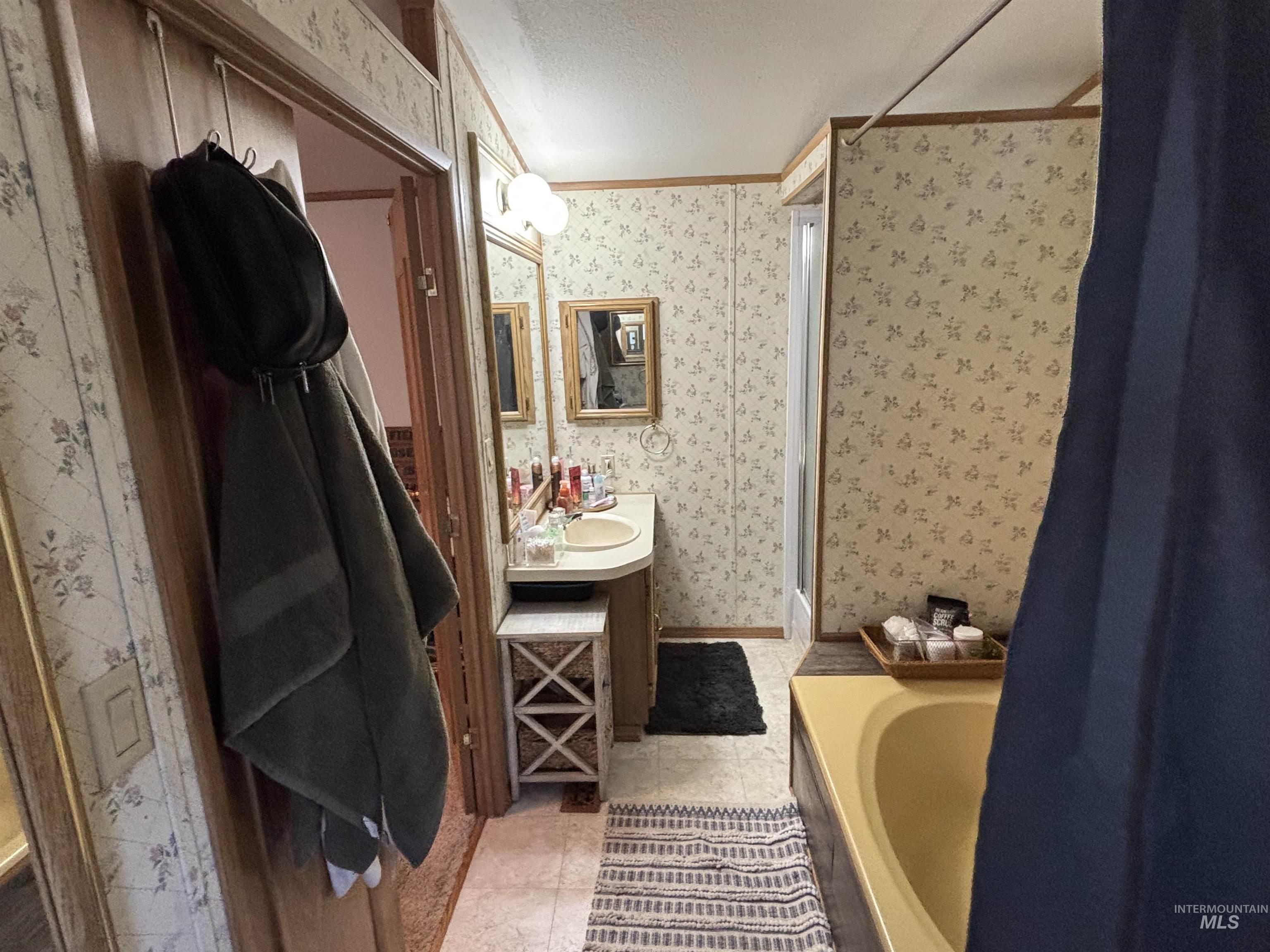 Bathroom featuring wallpapered walls, ornamental molding, vanity, a bathtub, and a textured ceiling