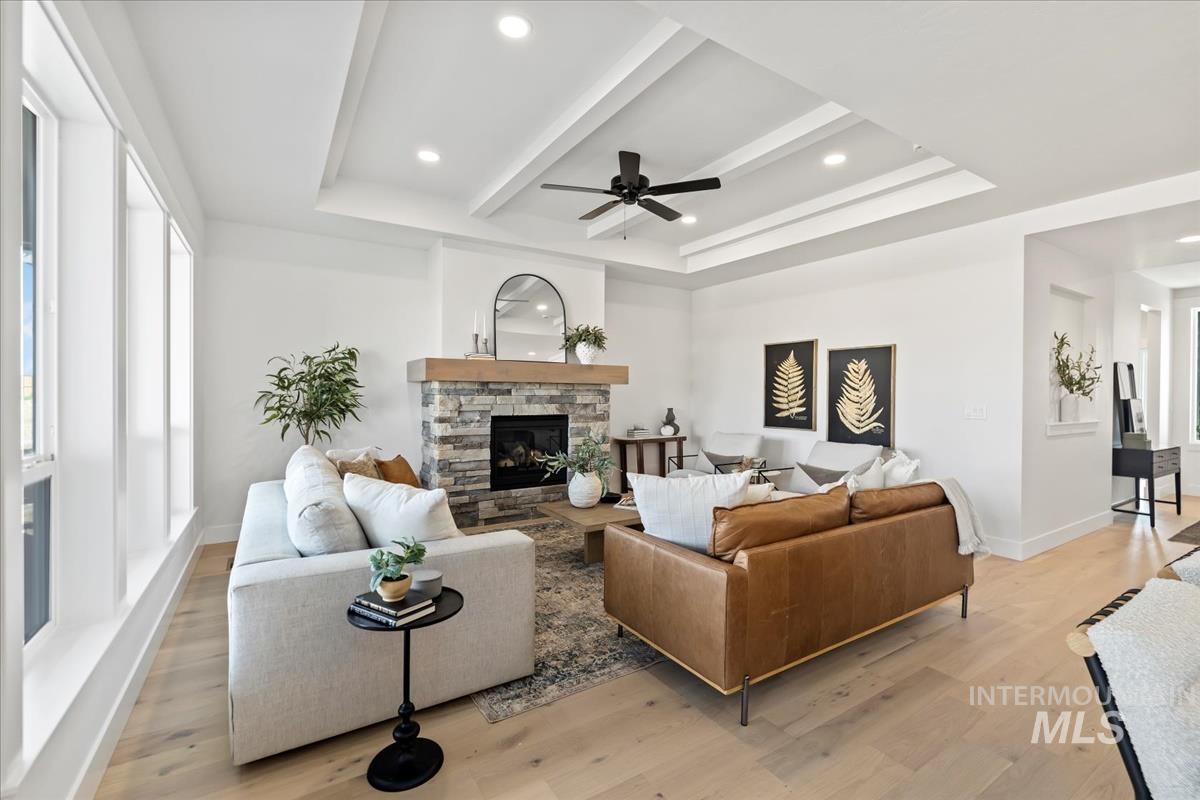 Living room featuring a stone fireplace, light wood-type flooring, ceiling fan, recessed lighting, and a raised ceiling