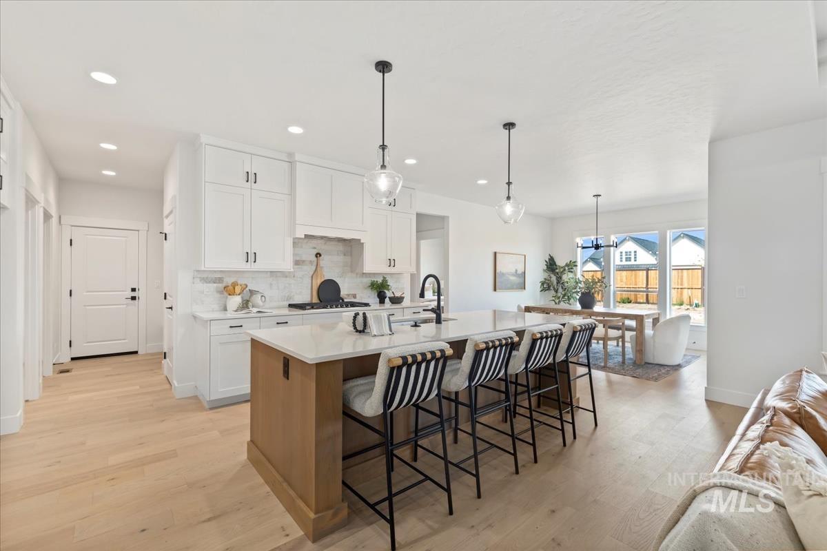 Kitchen featuring white cabinetry, a kitchen breakfast bar, a kitchen island with sink, pendant lighting, and light wood-style flooring