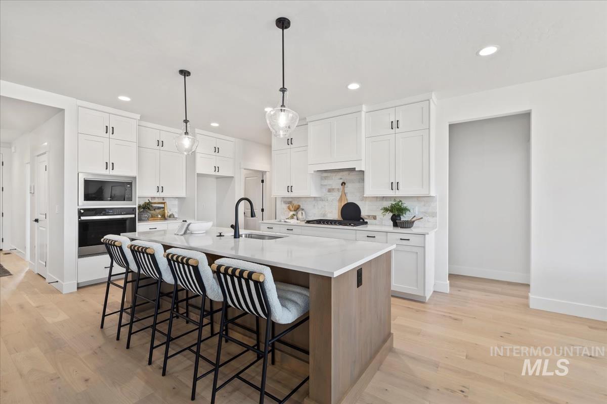 Kitchen with a breakfast bar, white cabinetry, decorative backsplash, oven, and an island with sink