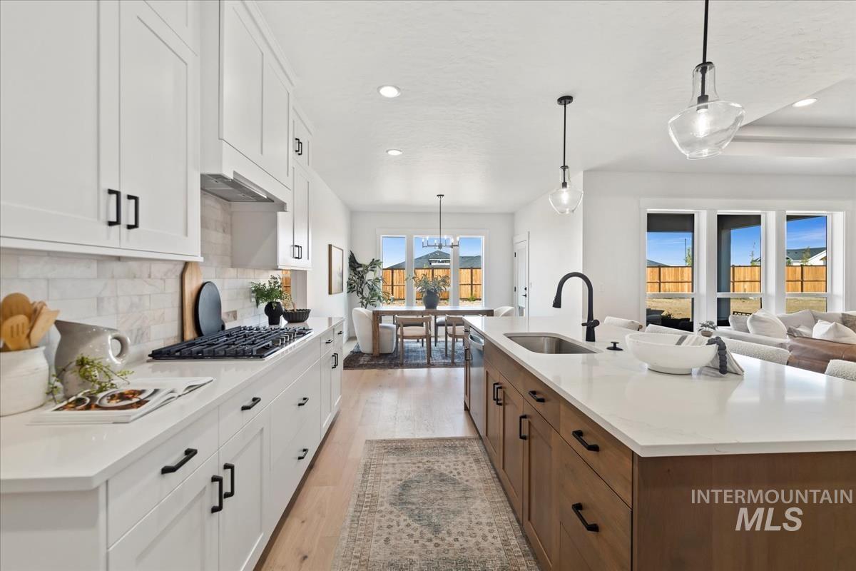 Kitchen with white cabinets, pendant lighting, light wood-style floors, decorative backsplash, and brown cabinets