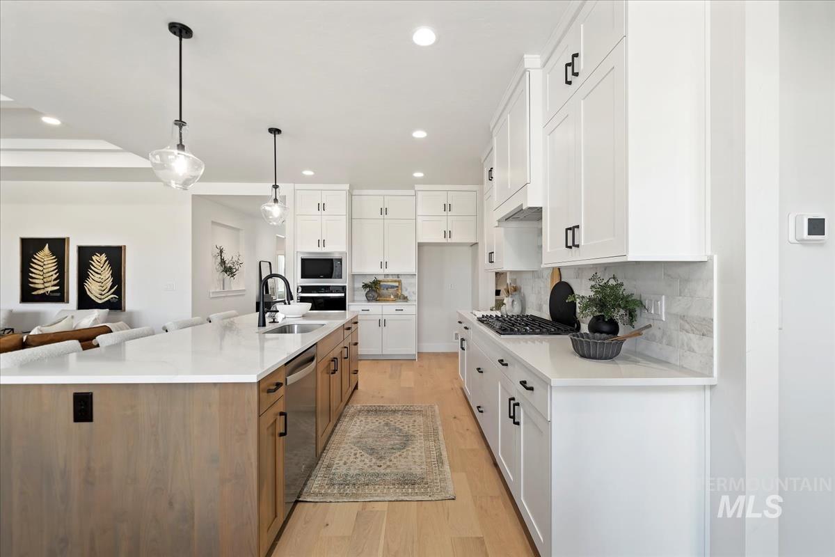 Kitchen featuring white cabinets, decorative light fixtures, tasteful backsplash, light stone countertops, and open floor plan