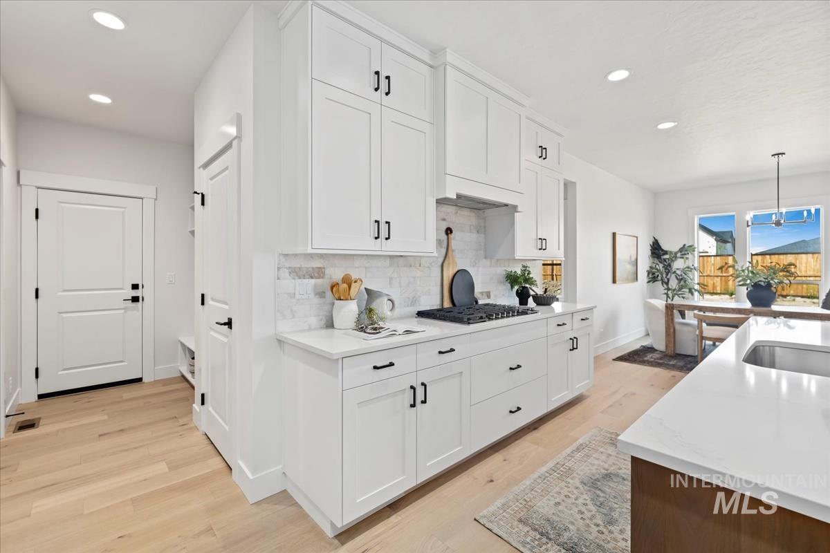 Kitchen with white cabinets, hanging light fixtures, recessed lighting, light stone countertops, and light wood finished floors