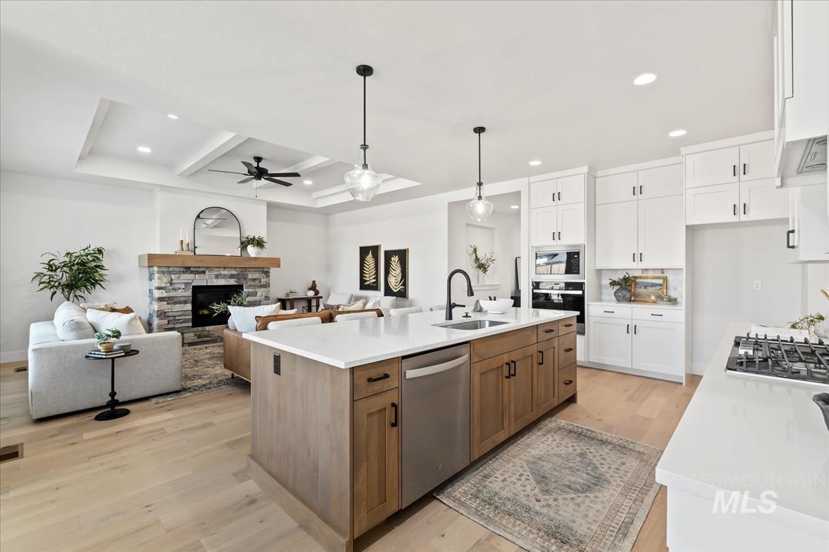 Kitchen with white cabinets, hanging light fixtures, light wood finished floors, brown cabinetry, and open floor plan