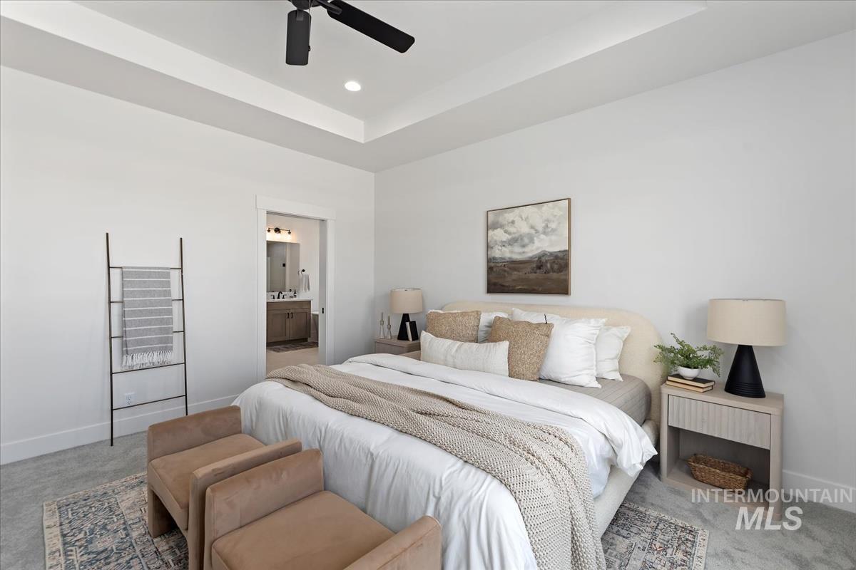 Carpeted bedroom with a raised ceiling, ensuite bath, ceiling fan, and recessed lighting