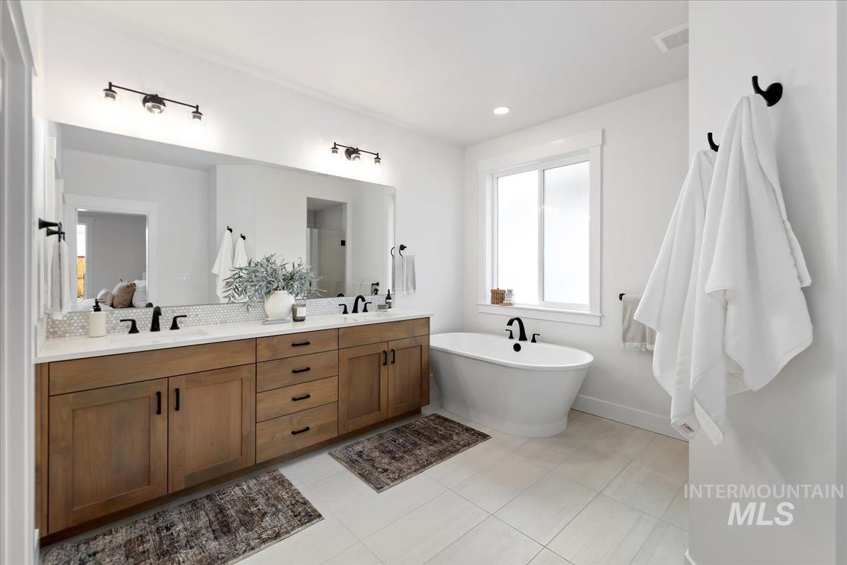 Bathroom with double vanity, a freestanding tub, light tile patterned floors, and ensuite bath