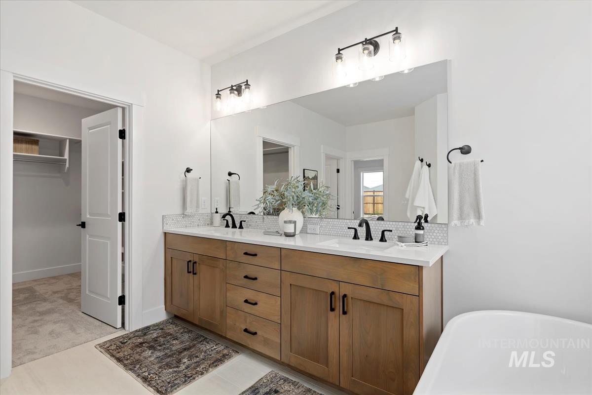 Full bathroom with a freestanding tub, a walk in closet, double vanity, light tile patterned floors, and tasteful backsplash
